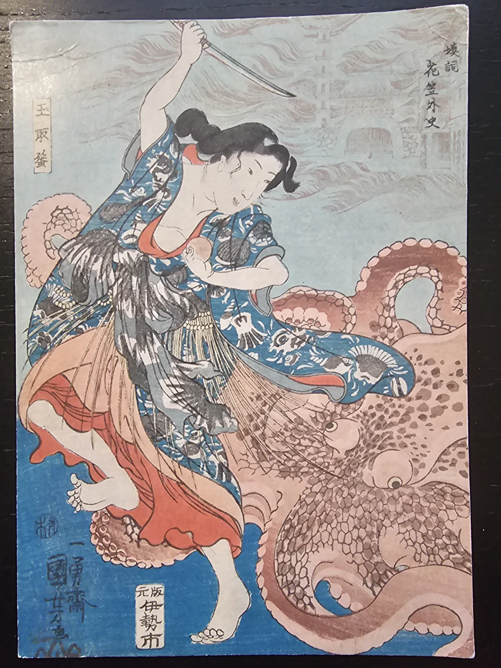 Ein farbiger japanischer Holzschnitt zeigt eine Frau mit erhobenem Schwert, die einen großen Oktopus bekämpft, dessen Tentakel sie umgeben.