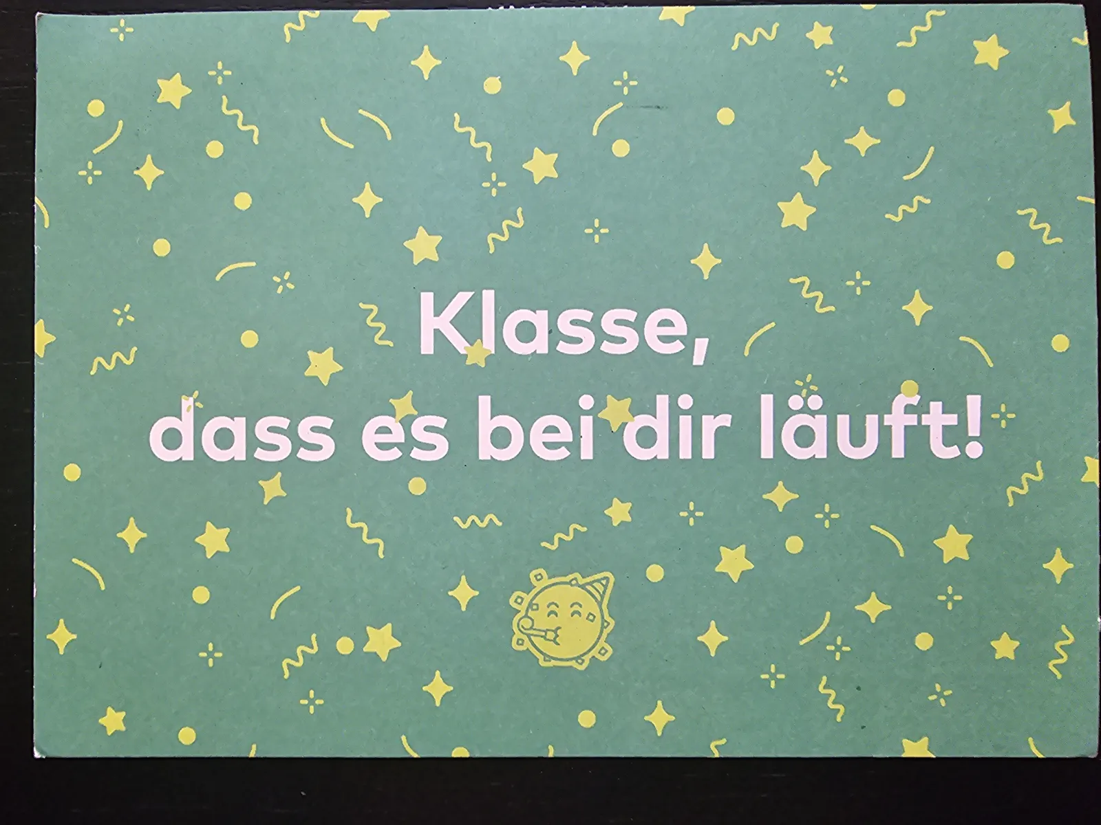 Eine grüne Karte mit gelben Konfetti-Motiven zeigt den weißen Text "Klasse, dass es bei dir läuft!" und ein lachendes Party-Sonne-Symbol.