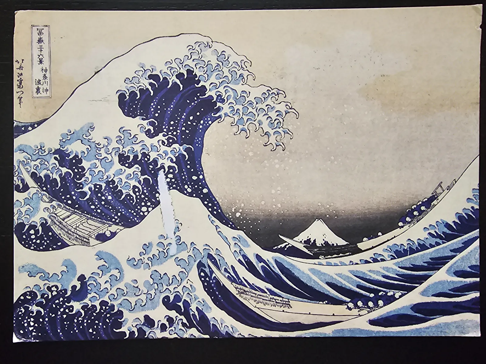 Die Große Welle von Hokusai: Eine riesige, schäumende blaue Welle füllt den Vordergrund, mit drei kleinen Booten, die in den Wellen kämpfen, und dem schneebedeckten Berg Fuji in der Ferne.