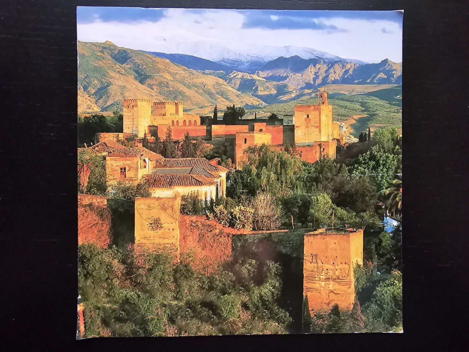 Die Alhambra, eine Festungsanlage aus rötlichen Gebäuden und Türmen, thront auf einem bewaldeten Hügel vor schneebedeckten Bergen.