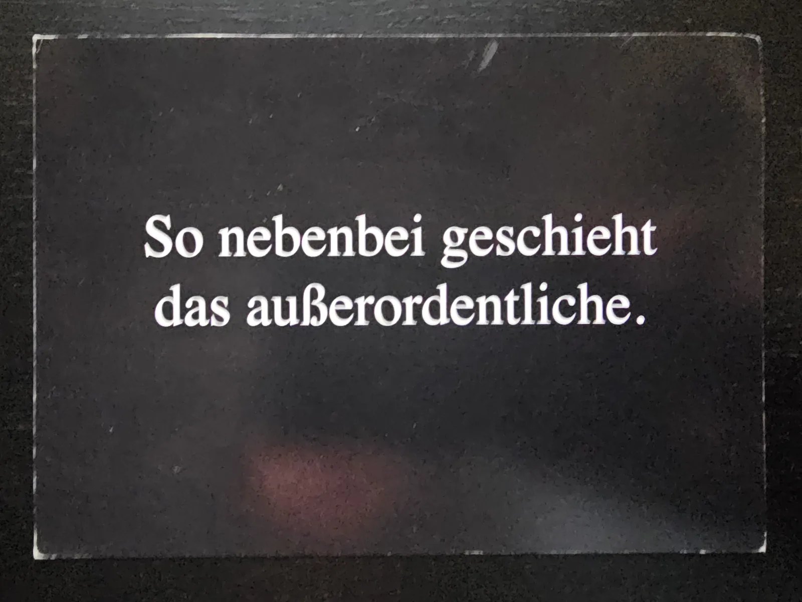 Eine dunkle Karte, auf der in weißer Schrift der Spruch: „So nebenbei geschieht das außerordentliche.“ steht.
