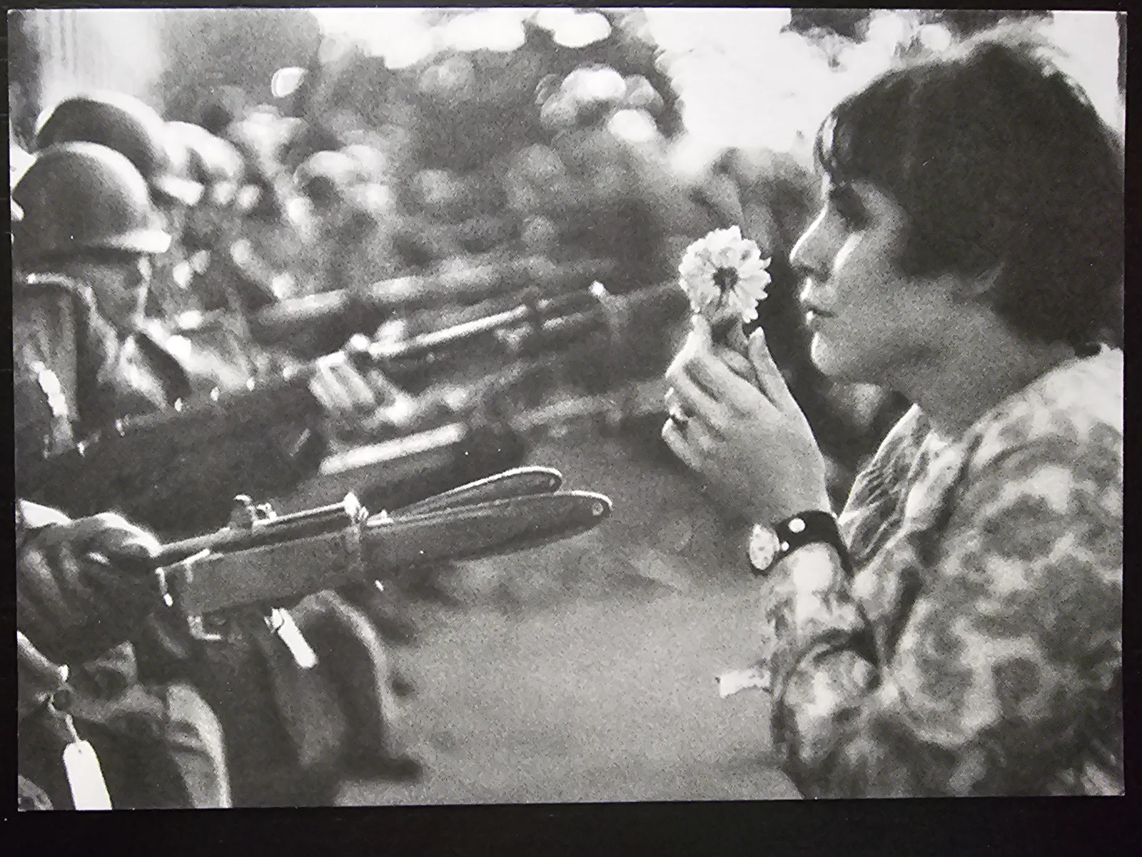 Eine Frau mit einer Blume in den Händen blickt einer Reihe von Soldaten mit aufgepflanzten Bajonetten entgegen.