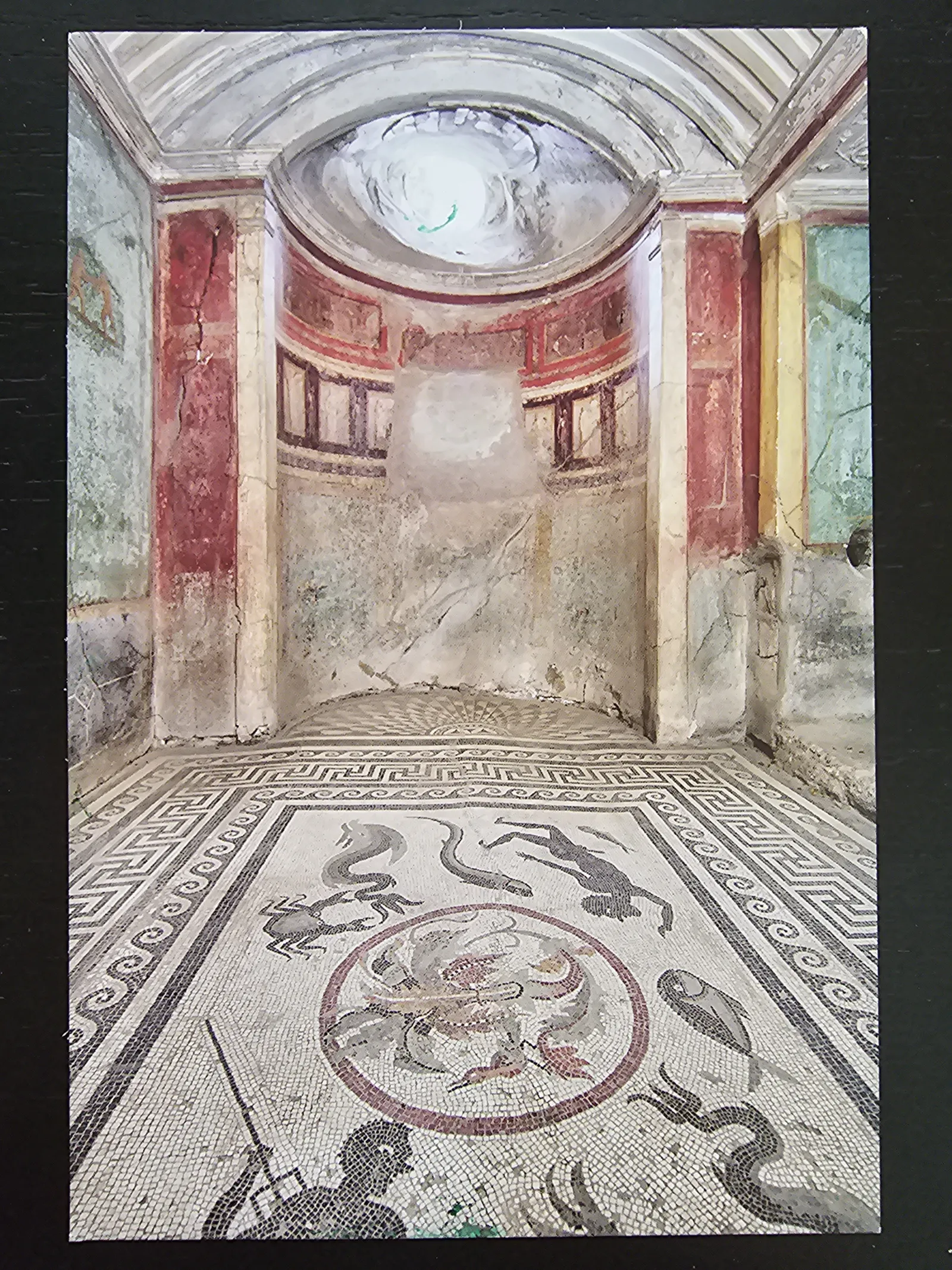 Ein antiker Raum mit einem Mosaikboden, der Meerestiere und geometrische Muster zeigt, sowie verblassten Fresken an den Wänden und einer gewölbten Nische.