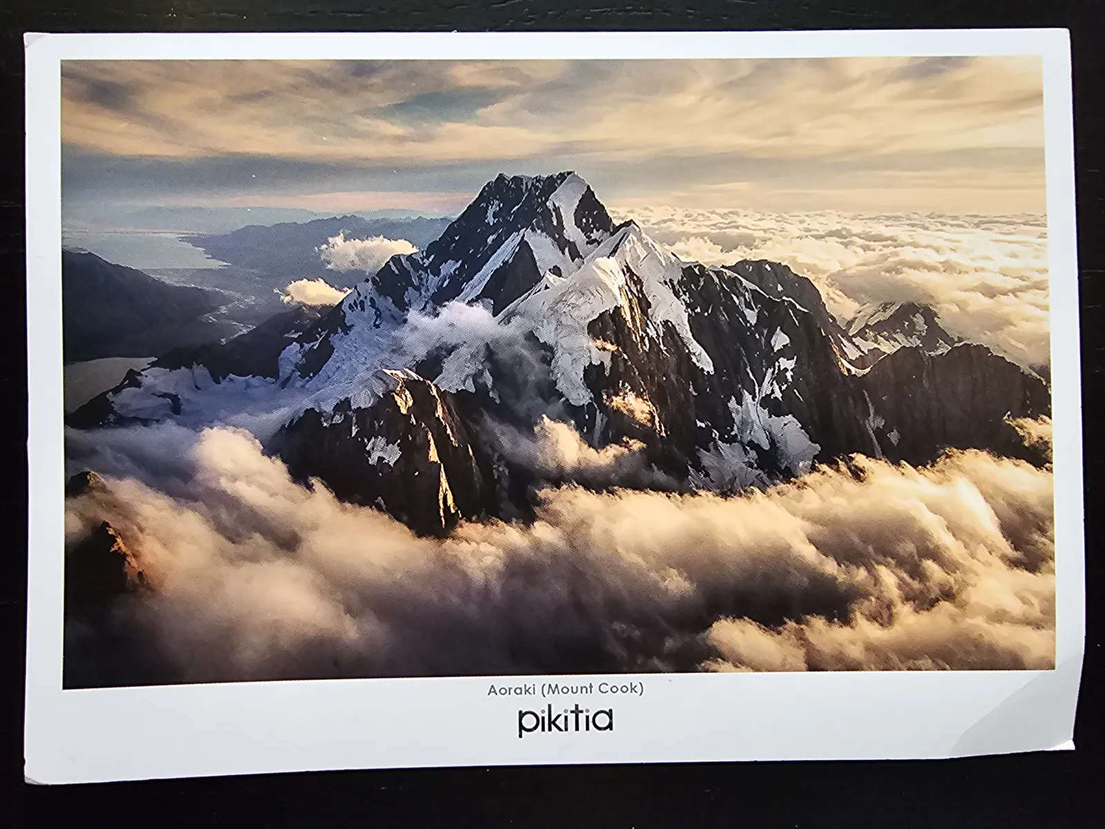 Der schneebedeckte Aoraki (Mount Cook) ragt im goldenen Licht über eine Wolkendecke.