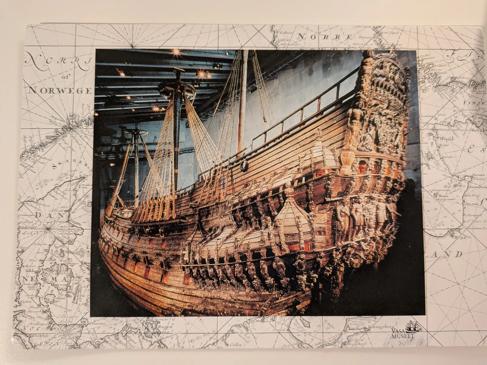Ein großes, reich geschnitztes Holzschiff, die Vasa, ist in einem Museum ausgestellt und von einer historischen Seekarte umgeben.