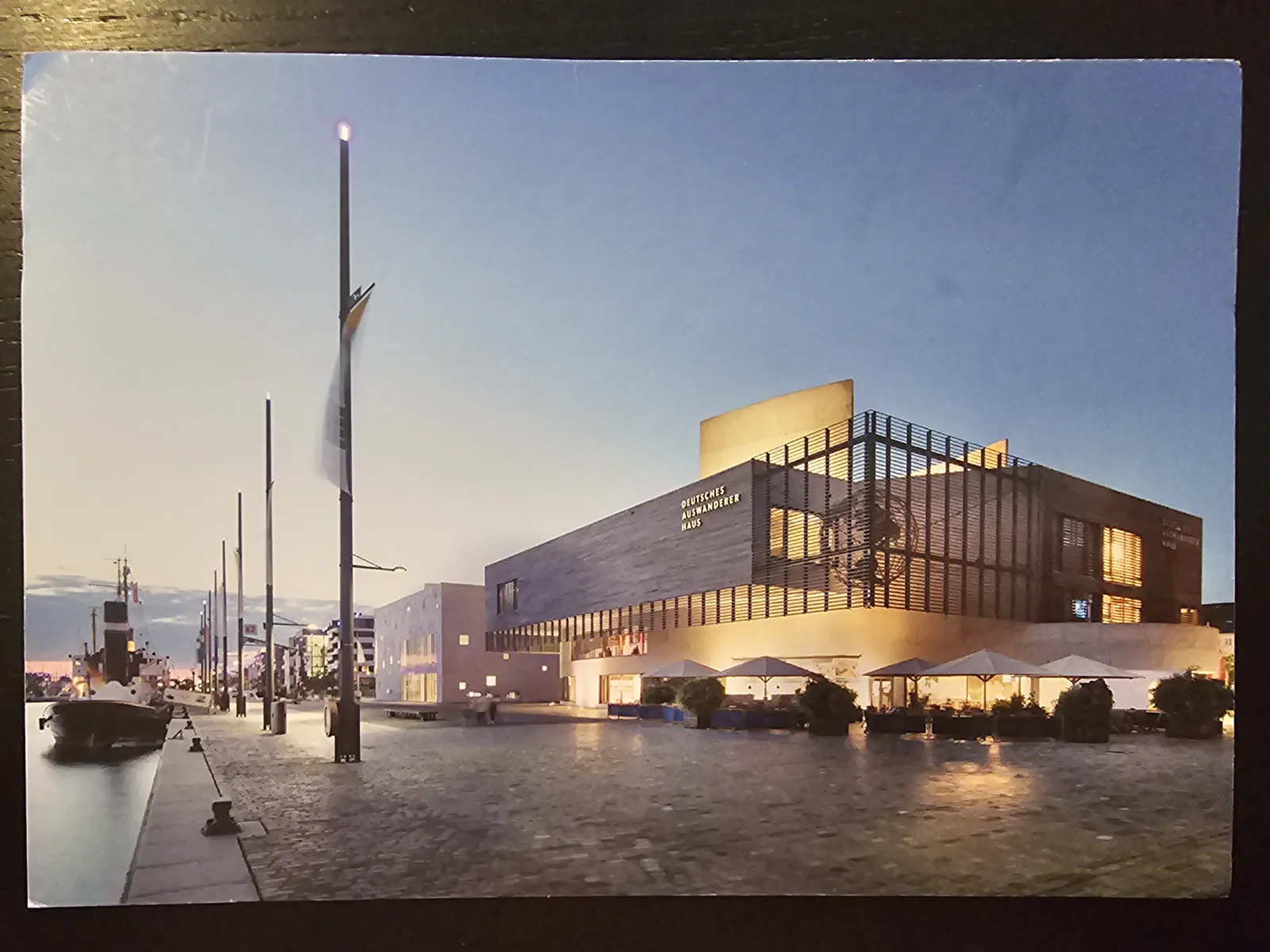 Abendliche Ansicht des modern beleuchteten Deutschen Auswanderer Hauses am Hafen mit einer Promenade und Außenterrassen.