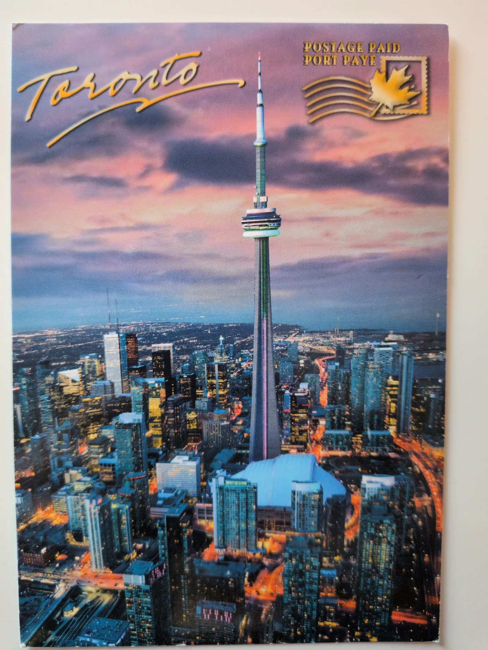 Dieses Bild ist eine Nachtansicht von Toronto mit dem CN Tower und beleuchteten Wolkenkratzern, ergänzt durch den Schriftzug „Toronto“ und einen kanadischen Frankierstempel.
