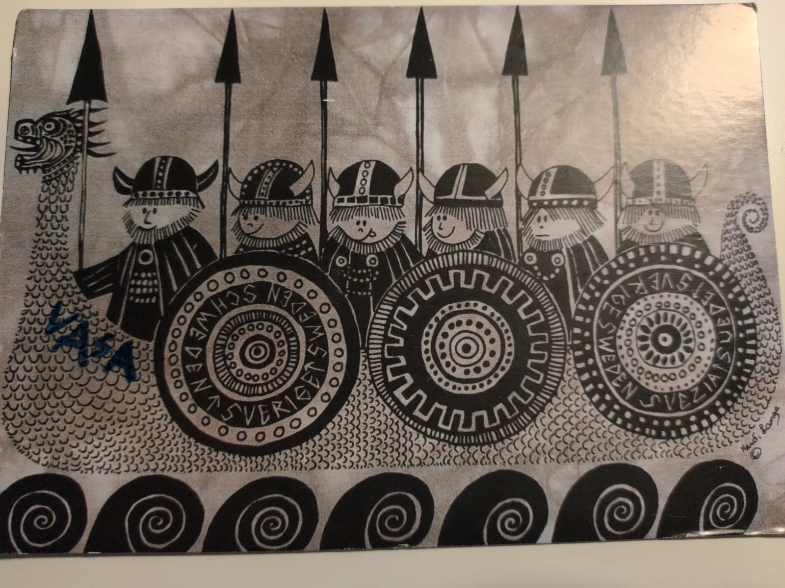 Ein stilisiertes, schwarz-weißes Bild zeigt ein Wikingerschiff mit Drachenkopf und sechs comicartigen Wikingern, die Speere und gemusterte Schilde mit der Aufschrift „SVERIGE“ tragen.