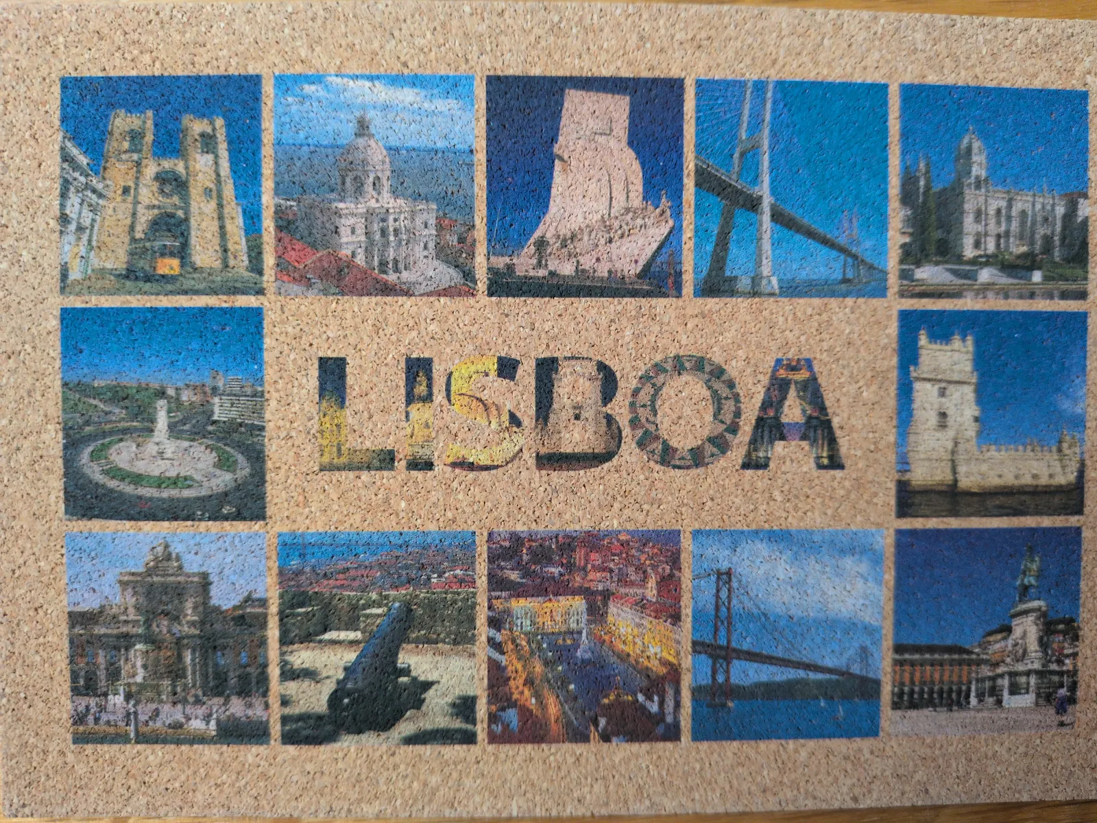 Eine Korkplatte zeigt eine Collage aus zwölf Bildern von Lissabonner Sehenswürdigkeiten, durch die mittig das Wort LISBOA ausgespart ist.