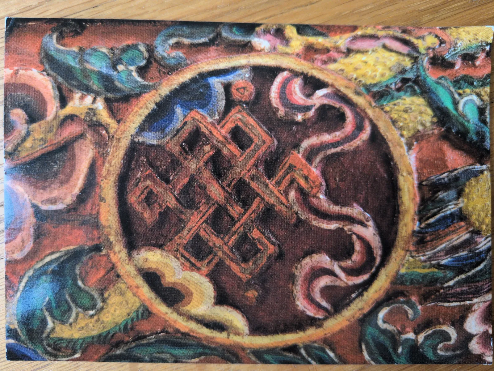 Das farbenprächtige Bild zeigt einen roten Endlosknoten in einem zentralen Kreis, umgeben von wirbelnden Mustern in Gelb, Grün und Blau.