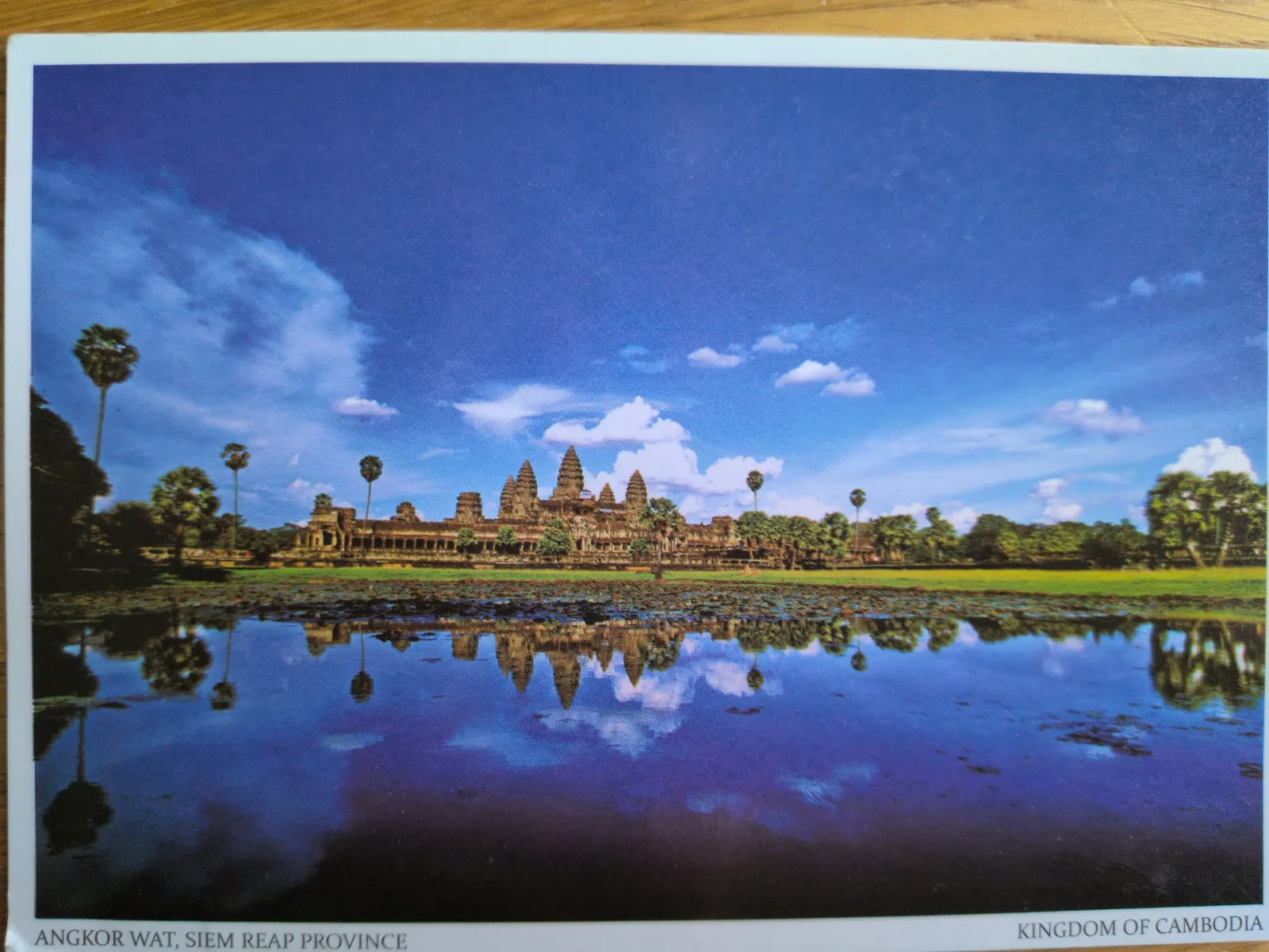 Angkor Wat mit seinen Türmen und Palmen spiegelt sich unter blauem Himmel in einem See.