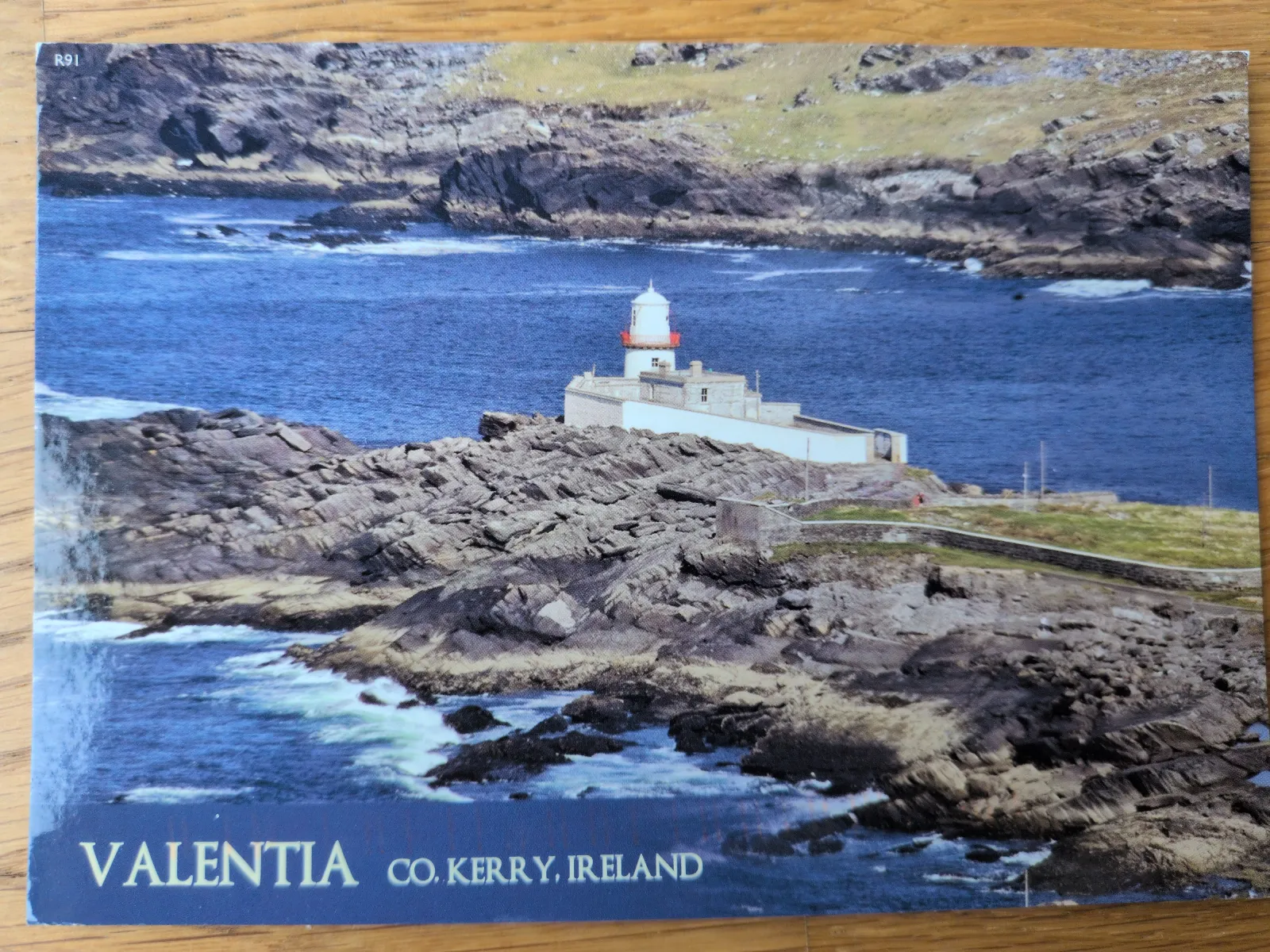 Ein weißer Leuchtturm mit rotem Dach steht auf einer felsigen Küste am blauen Meer in Valentia, Irland.