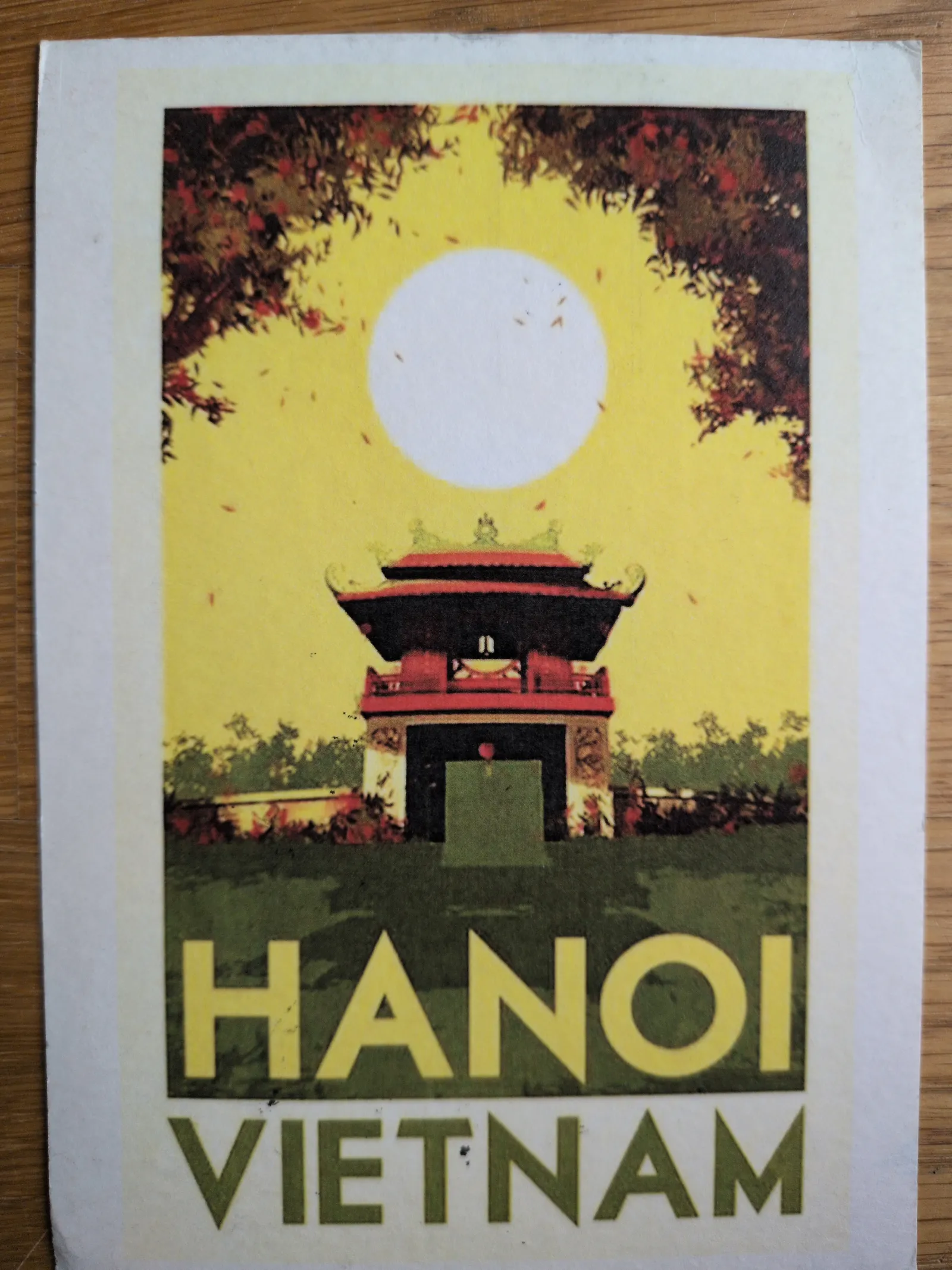 Ein stilisiertes Reiseplakat für Hanoi, Vietnam, zeigt ein rotes Tempelgebäude vor gelbem Himmel mit einer großen weißen Sonne und dunklen Bäumen.