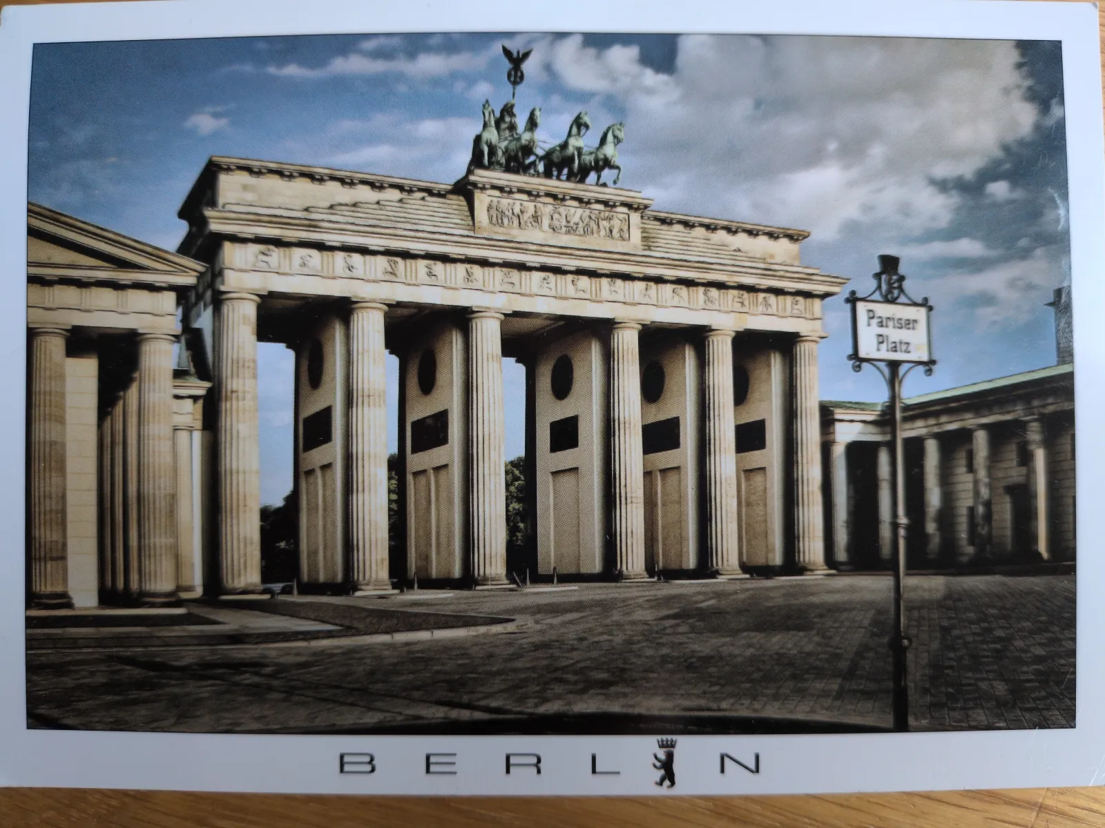 Das Bild zeigt das Brandenburger Tor in Berlin mit der Quadriga auf dem Dach und einem Schild zum Pariser Platz.