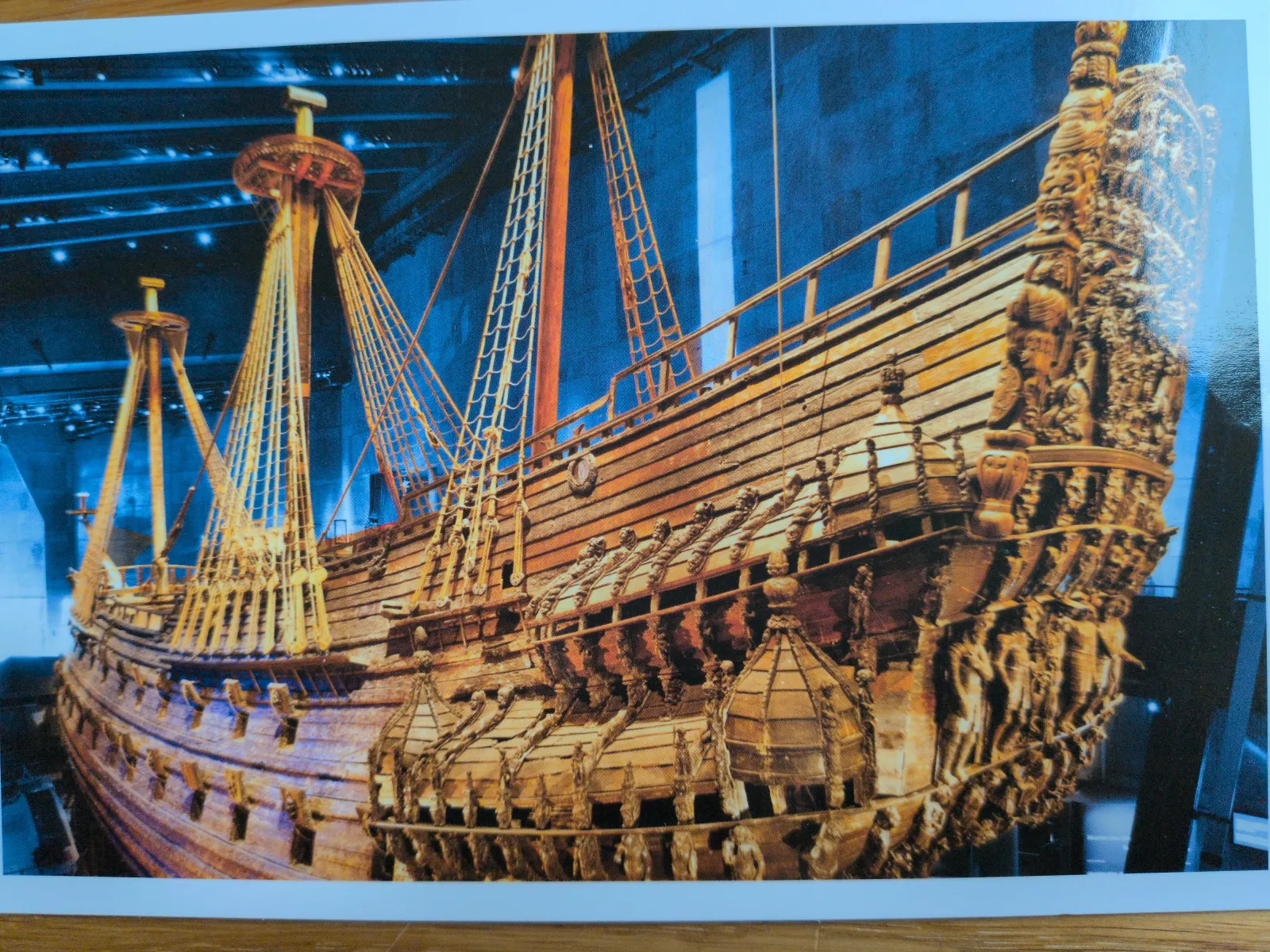 Ein prunkvolles, altes Holzschiff mit hohen Masten und reichen Schnitzereien am Heck ist in einem bläulich beleuchteten Museum ausgestellt. Das Bild zeigt die Vasa.