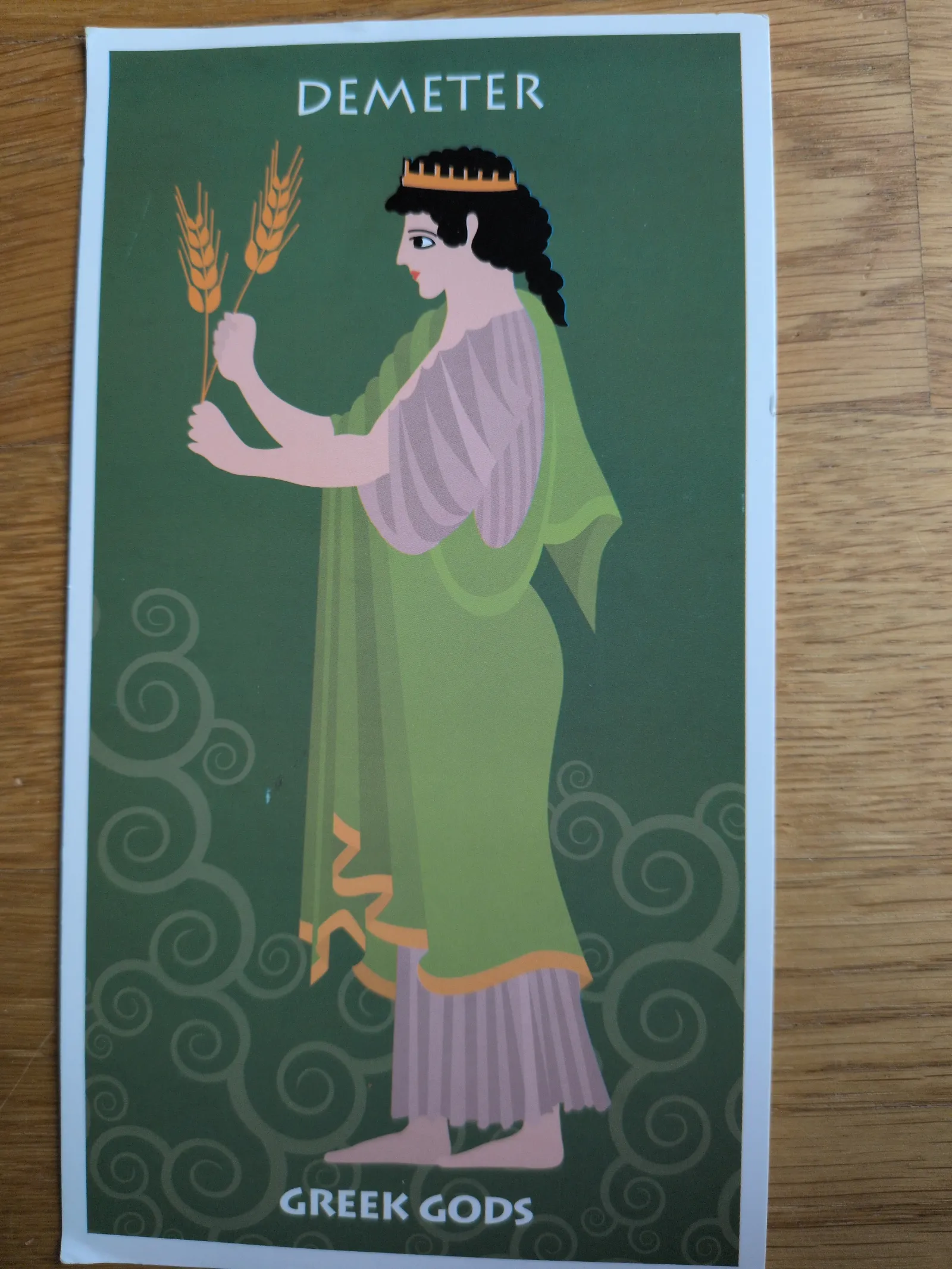 Eine stilisierte Illustration der Göttin Demeter mit goldener Krone, grünem Gewand und zwei Weizenähren in den Händen.