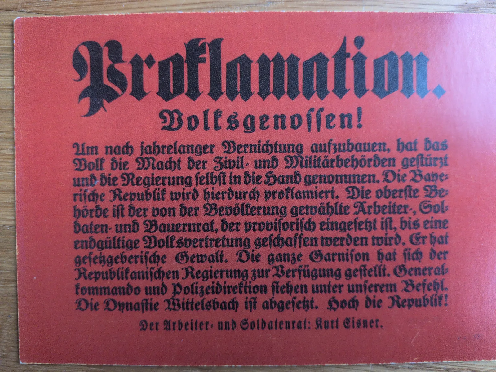 Rotes Dokument mit schwarzer Frakturschrift, das die Proklamation der Bayerischen Republik durch Kurt Eisner verkündet.