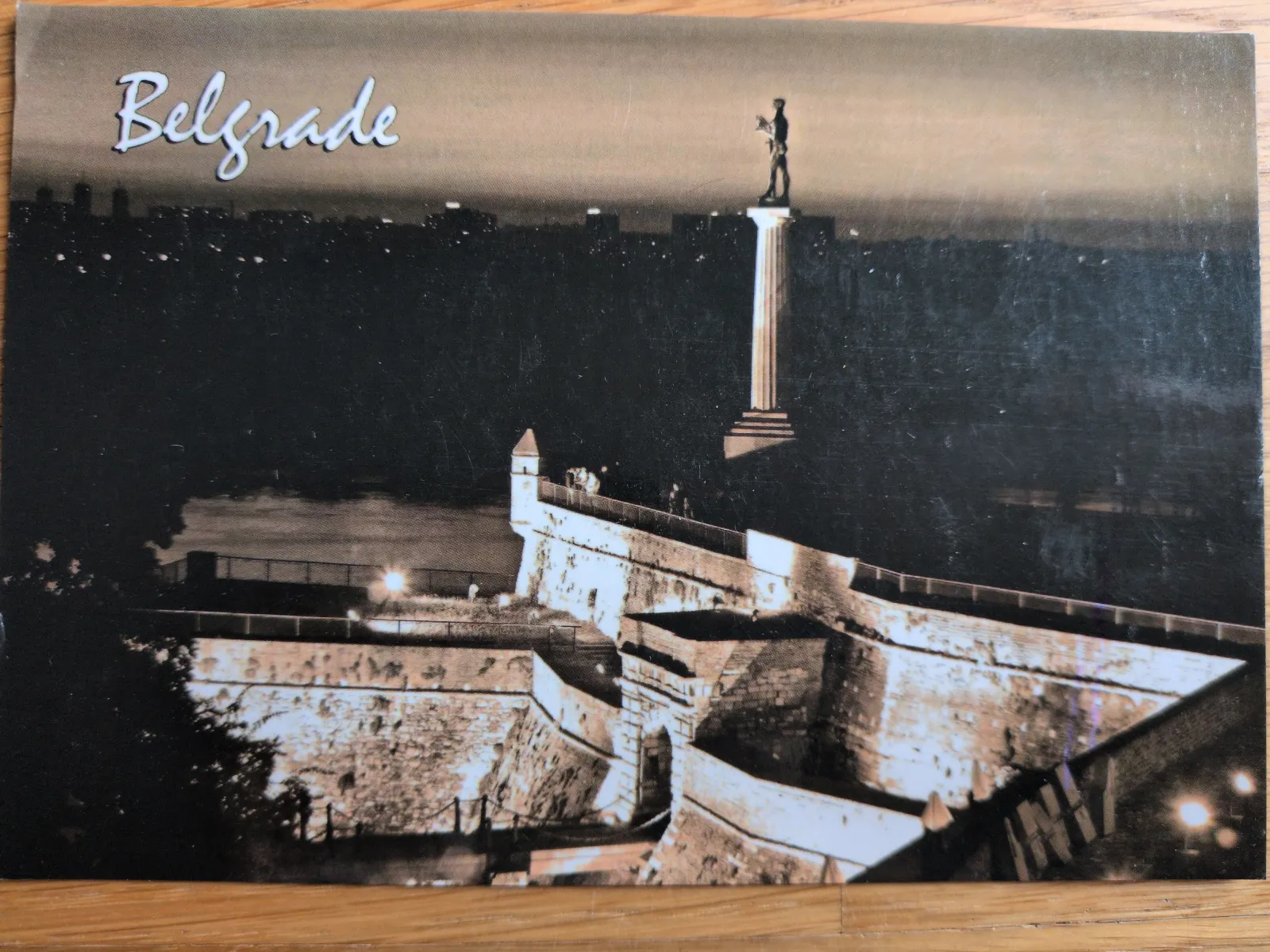 Das Bild zeigt eine nächtliche Ansicht von Belgrad mit einer Statue auf einer Säule über einer Festung.