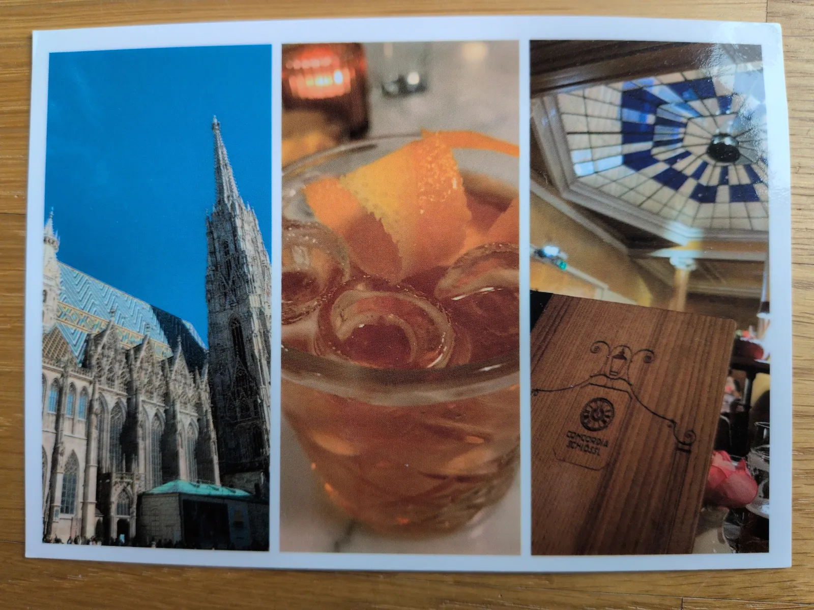Das Bild zeigt den Stephansdom, ein Getränk mit Orange und Eis, und eine Holzspeisekarte unter einer blauen Kuppel.