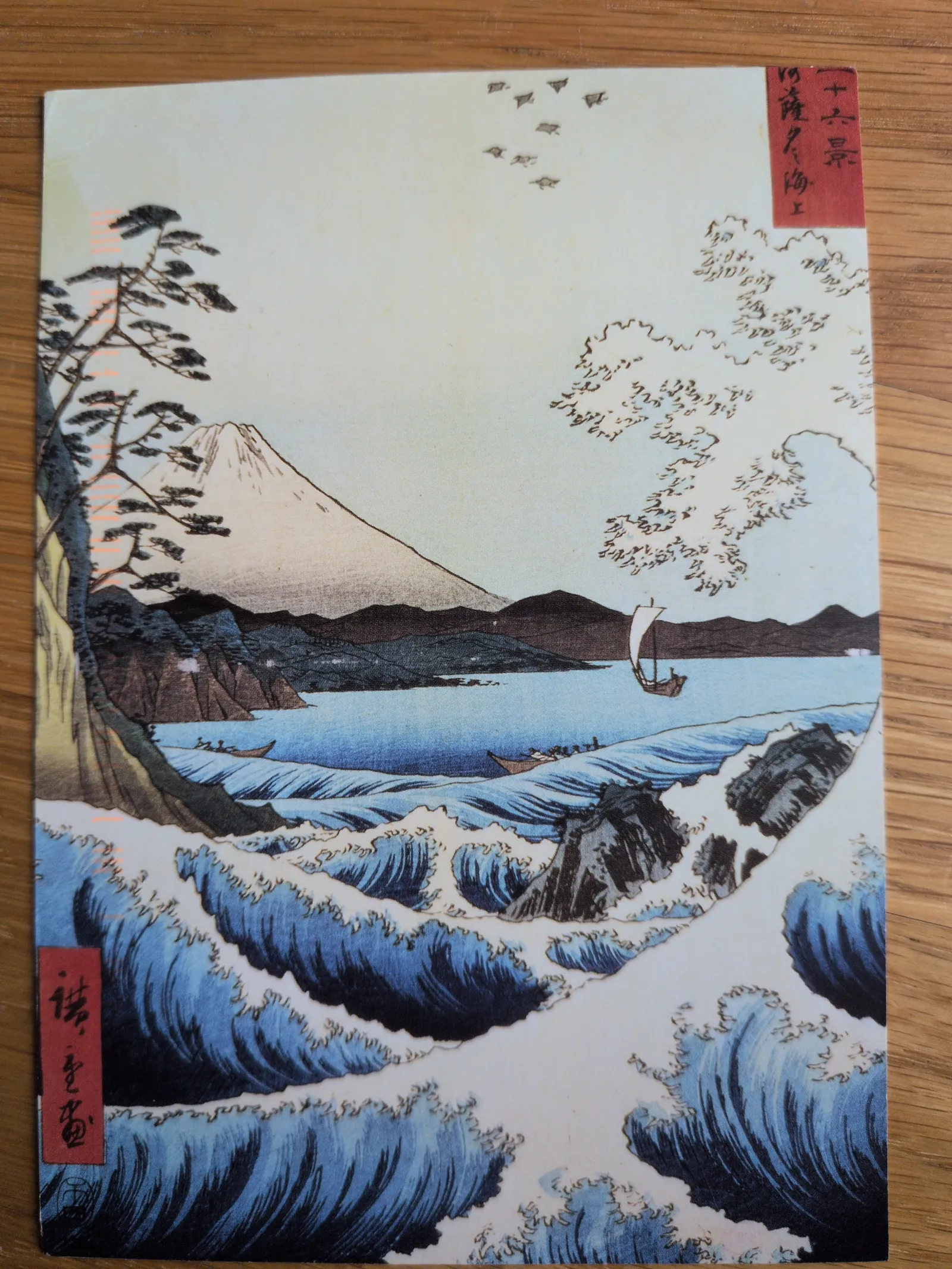 Ein japanischer Farbholzschnitt zeigt eine riesige blaue Welle im Vordergrund, die über Fischerboote hereinbricht, mit dem schneebedeckten Berg Fuji in der Ferne.