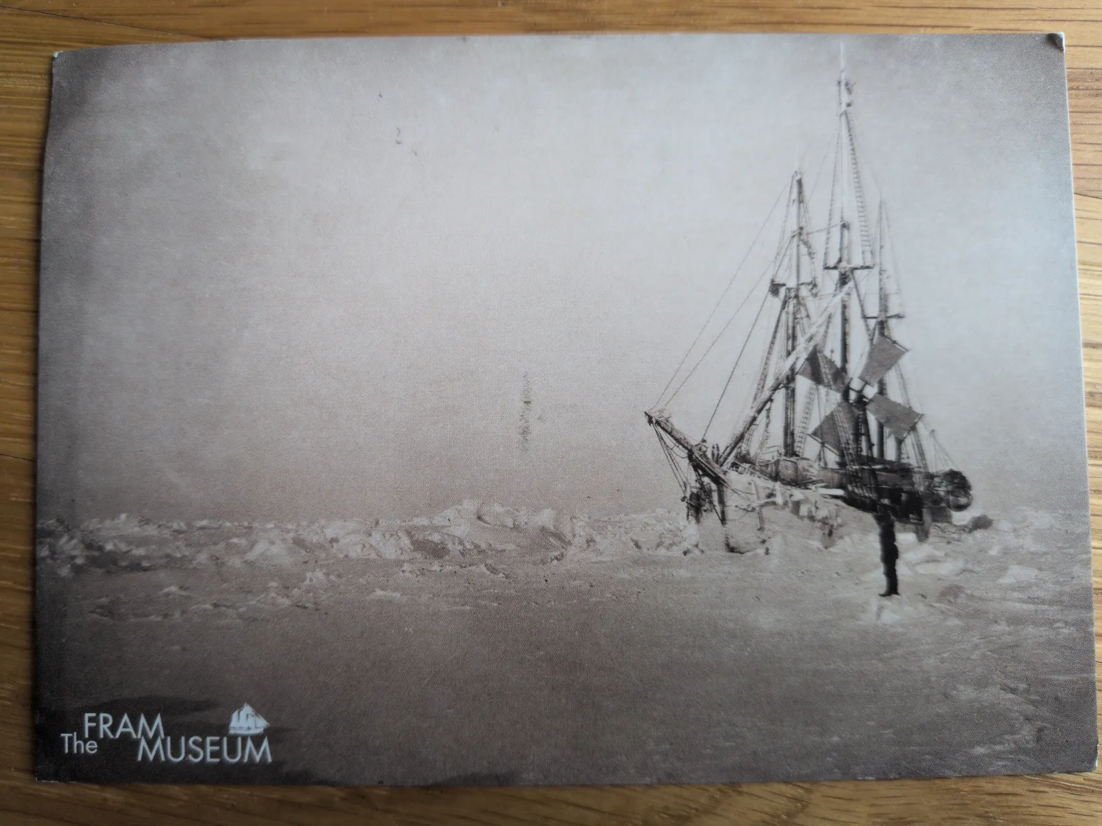 Ein altes, sepiafarbenes Foto zeigt ein Segelschiff, das schräg im Packeis feststeckt.