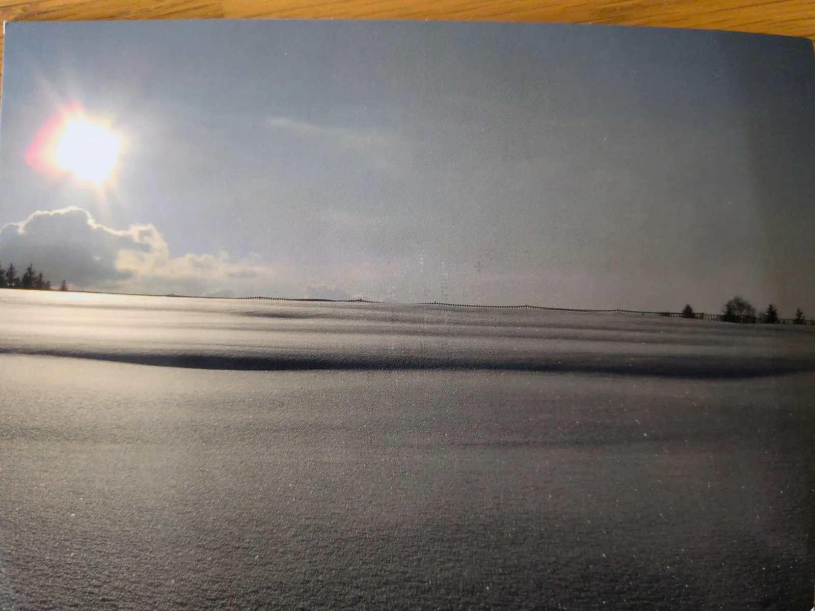 Ein sonniges Landschaftsfoto zeigt einen See oder das Meer unter blauem Himmel mit der strahlenden Sonne und einer fernen Uferlinie.