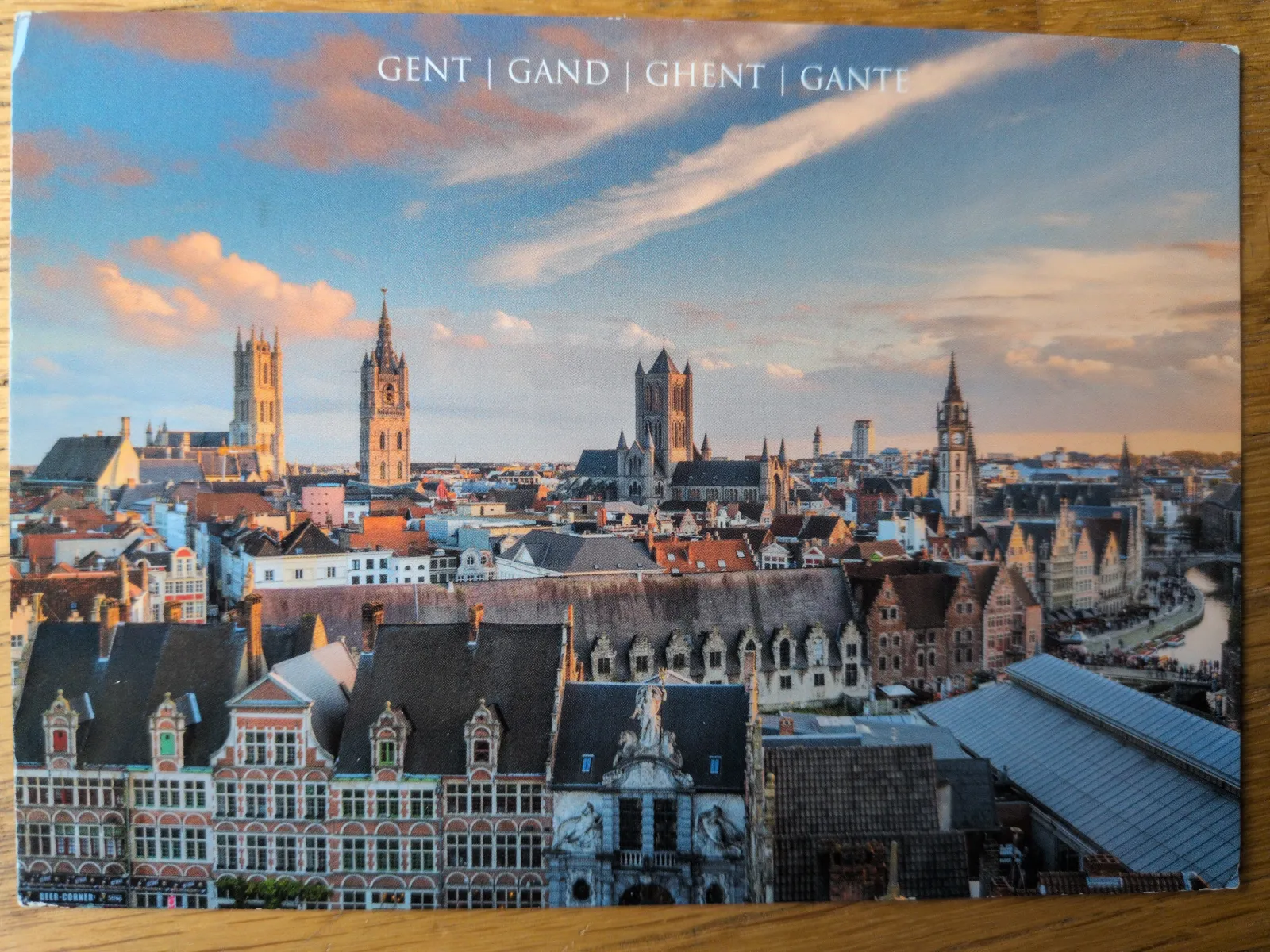 Eine weite Ansicht der Stadt Gent zeigt zahlreiche historische Gebäude, markante Türme und einen Fluss unter einem teils bewölkten Himmel.