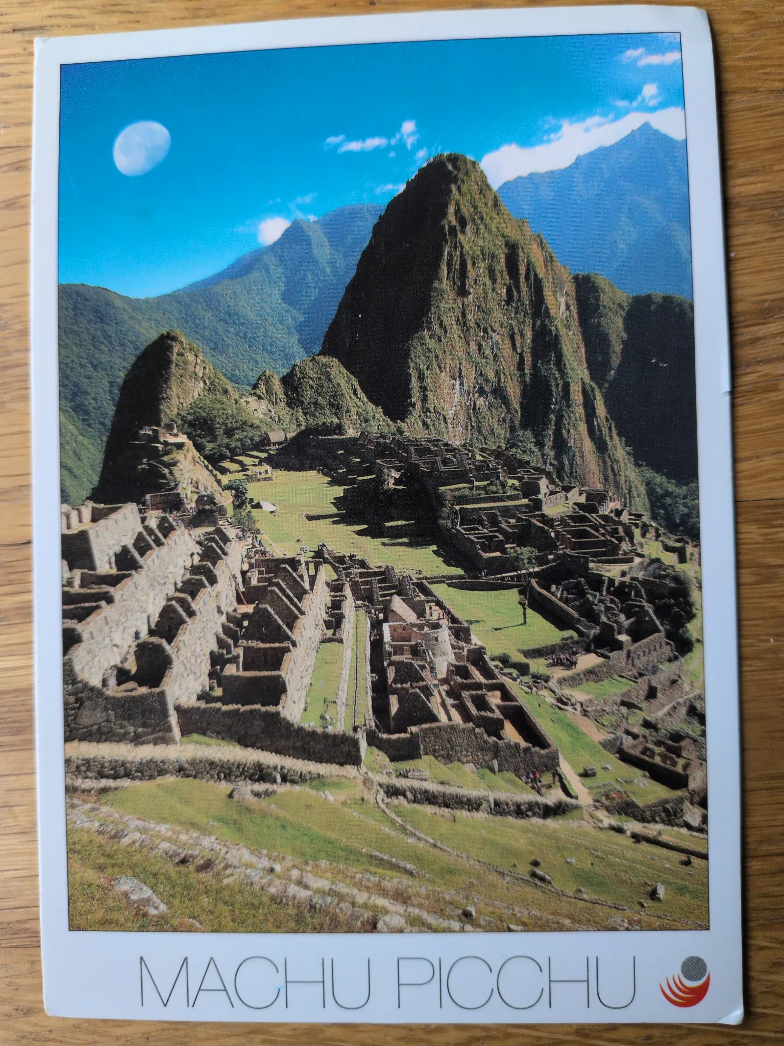 Machu Picchu, eine antike Inka-Stadt mit Steinterrassen und Gebäuden, liegt inmitten grüner Berge unter blauem Himmel mit Mond.