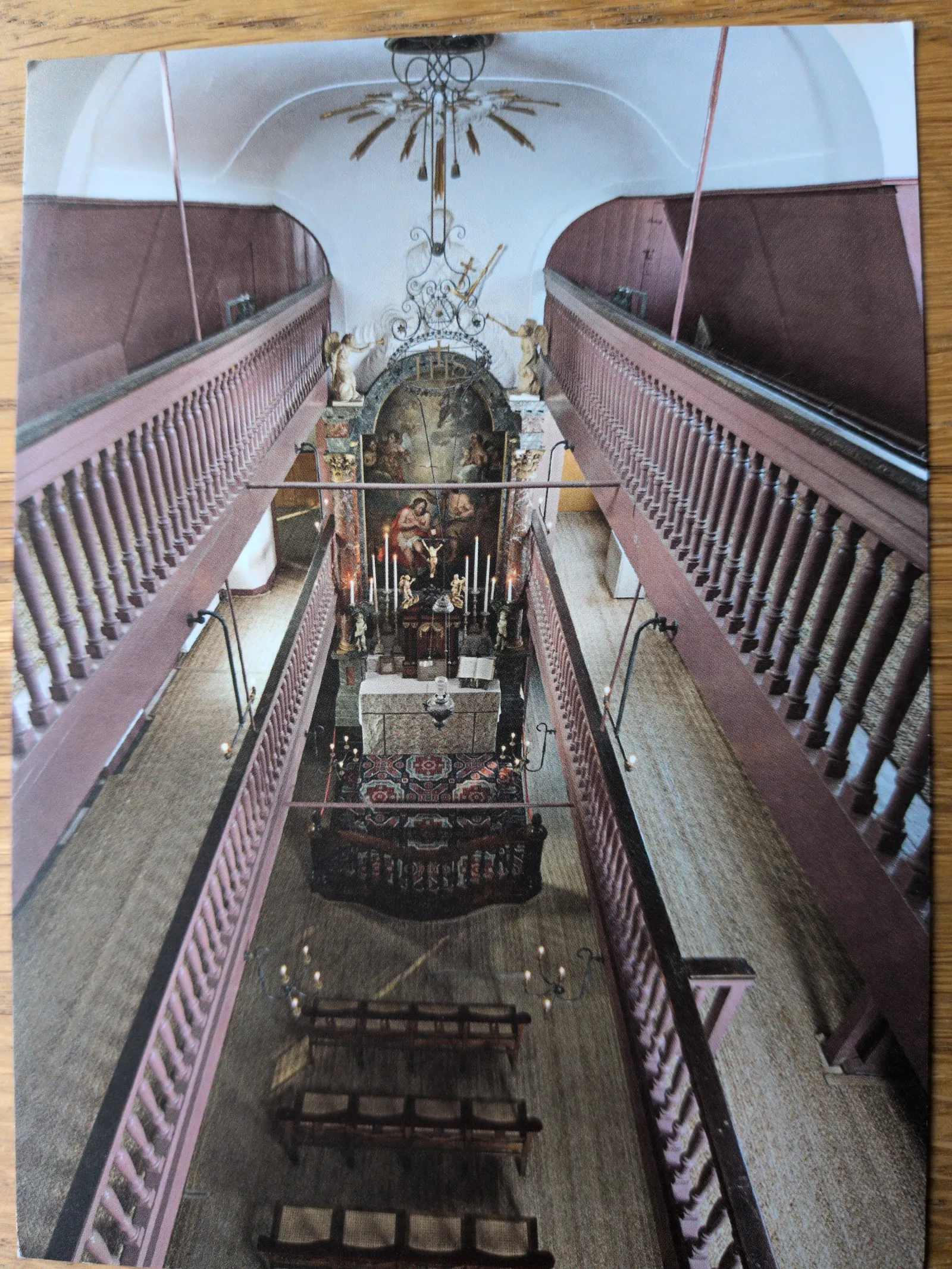 Eine Draufsicht in eine Kirche zeigt zwei lange, seitliche Treppen, die zu einem reich verzierten Altar mit Gemälde und Kerzen führen.