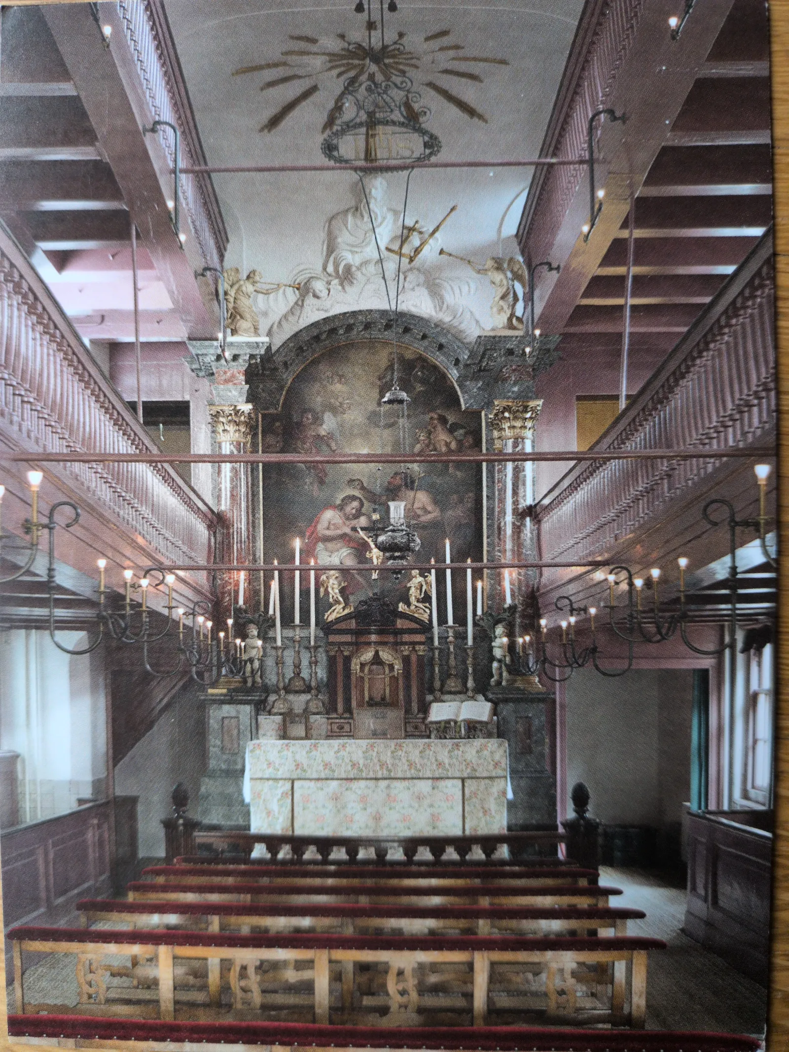 Ein reich verziertes Kirchenschiff mit Sitzreihen, einem großen Altarbild und seitlichen Emporen.