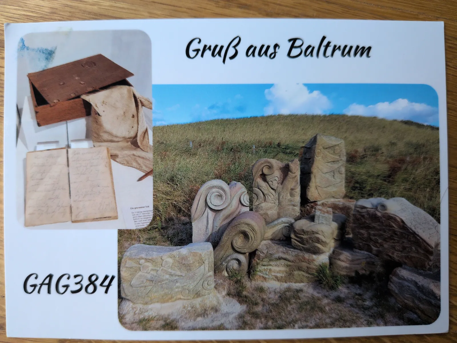 Eine Postkarte mit der Aufschrift „Gruß aus Baltrum“ zeigt eine Dünenlandschaft mit kunstvoll geschnitzten Steinen und ein kleineres Bild von alten Dokumenten in einer Holzkiste.