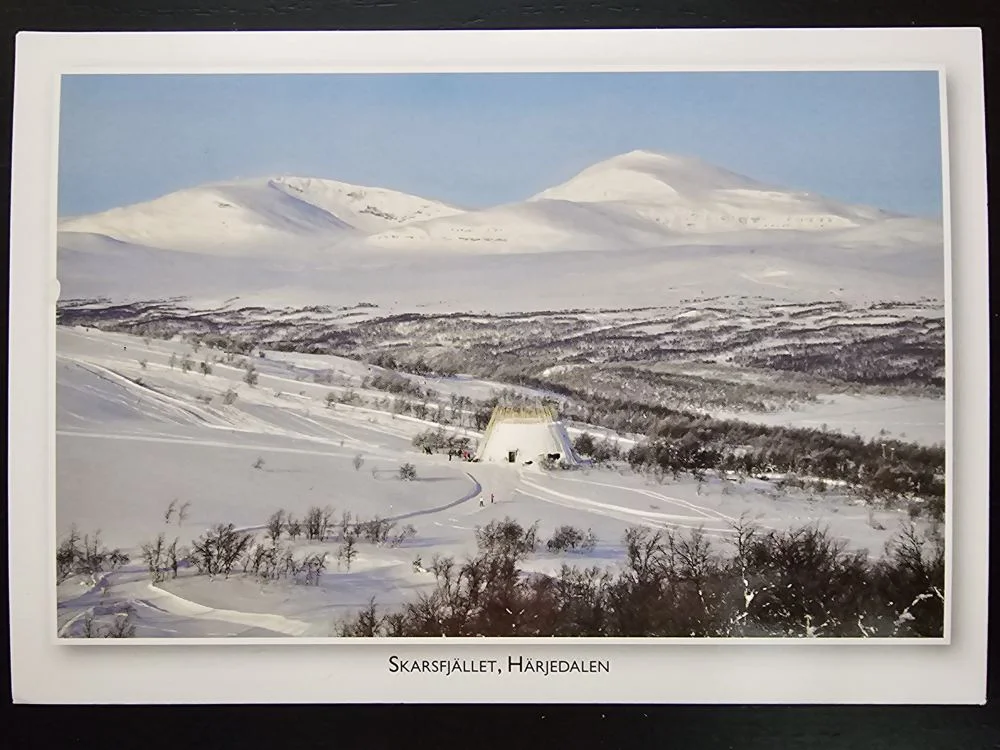 Ein weites, schneebedecktes Bergpanorama mit einem großen, zeltartigen Gebäude und Skifahrern auf den Hängen.