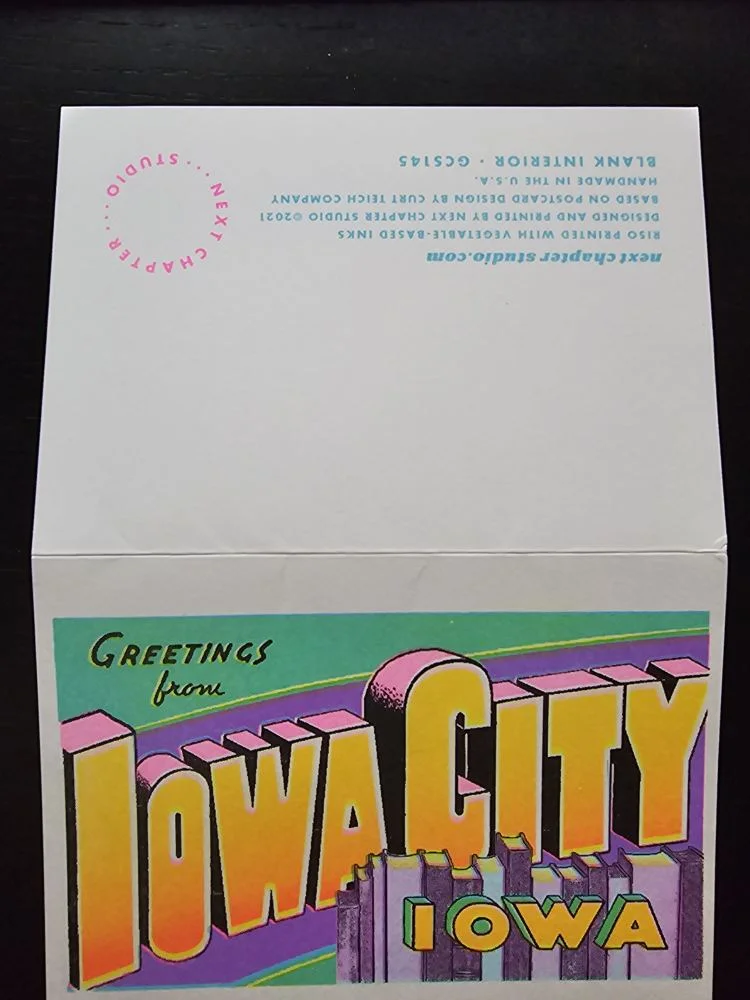 Eine geöffnete Grußkarte zeigt auf der unteren Hälfte eine farbenfrohe Vintage-Illustration mit den Worten „GREETINGS from IOWA CITY IOWA“ und auf der oberen Hälfte Herstellerangaben.