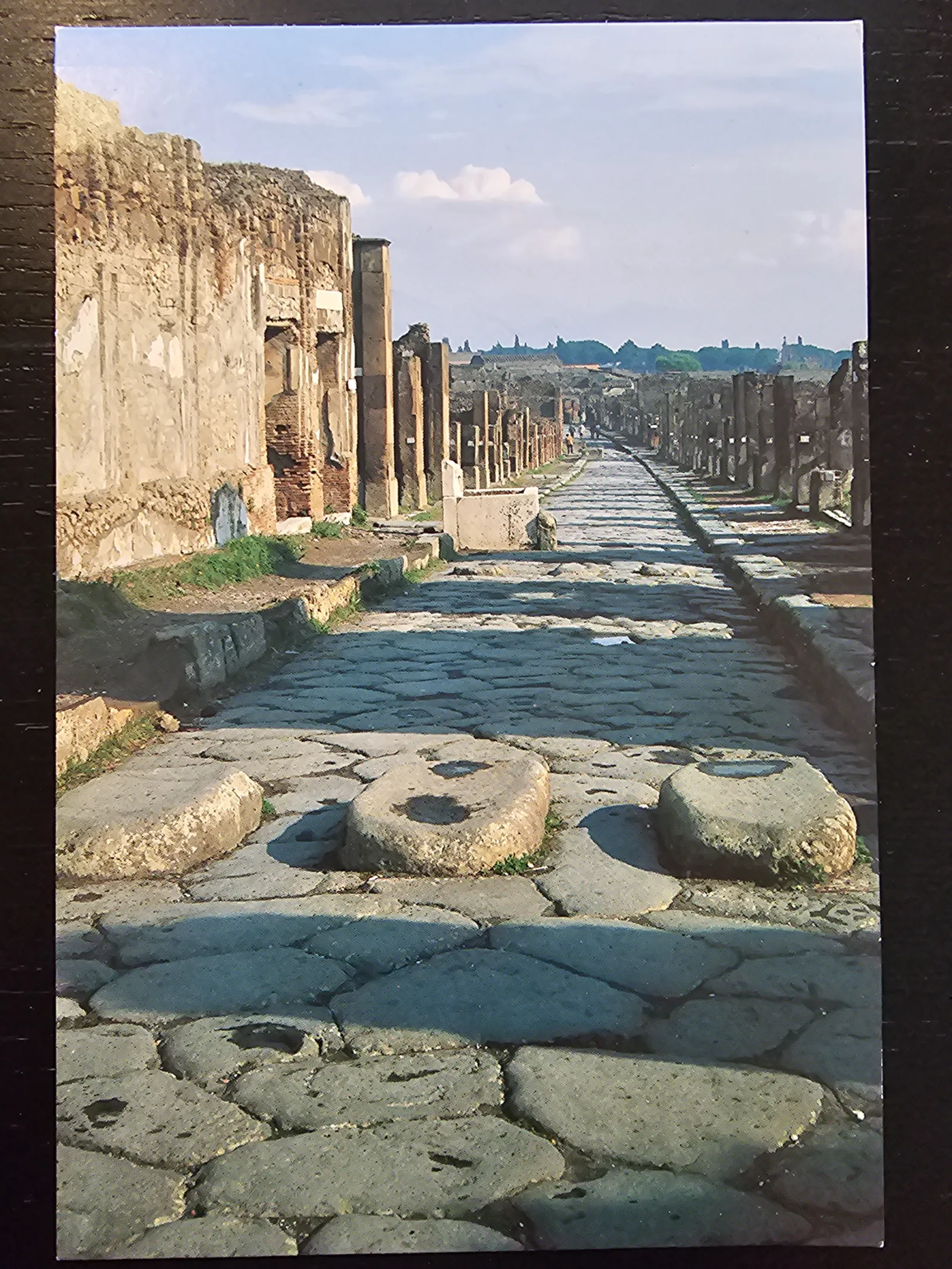 Eine lange, gepflasterte Straße in antiken Ruinen erstreckt sich in die Ferne, gesäumt von Gebäuderesten und mit großen Trittsteinen im Vordergrund.