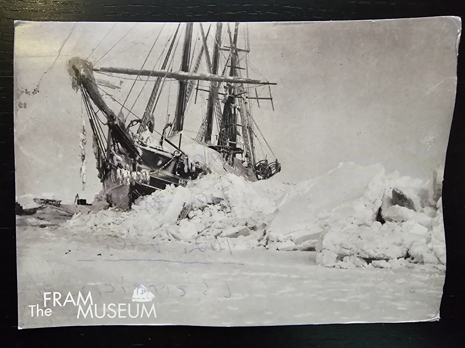 Ein Schwarz-Weiß-Foto zeigt ein großes Segelschiff, das schräg in einem Meer aus aufgetürmten Eisschollen feststeckt.