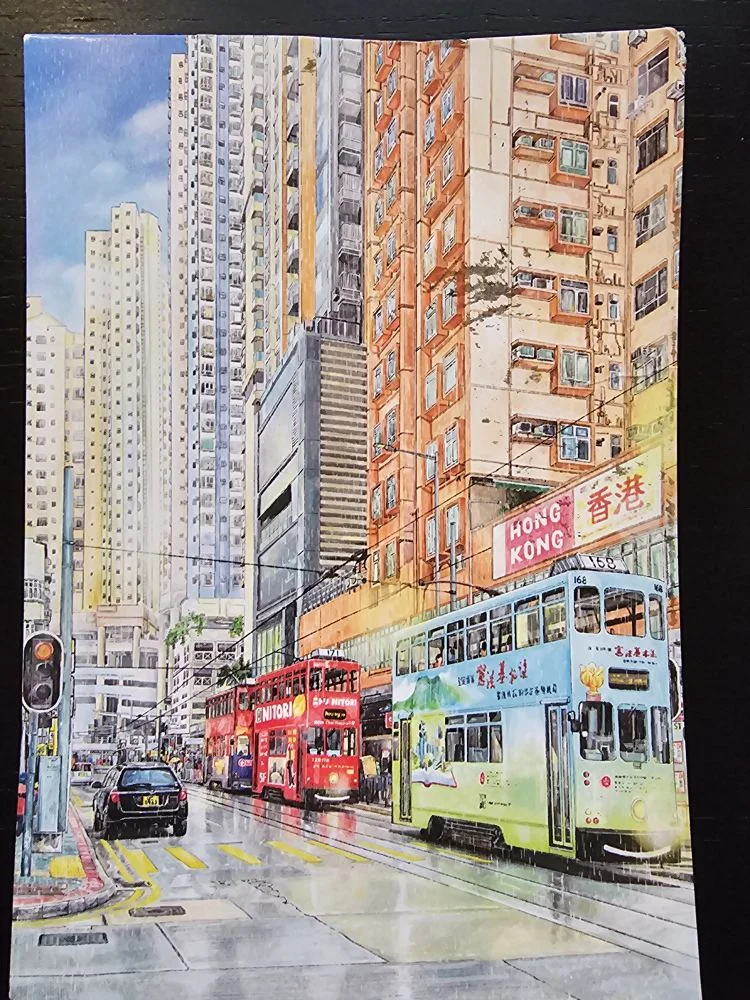 Ein farbenfrohes Stadtbild von Hongkong zeigt hohe Gebäude, zwei doppelstöckige Straßenbahnen und eine nasse Straße.