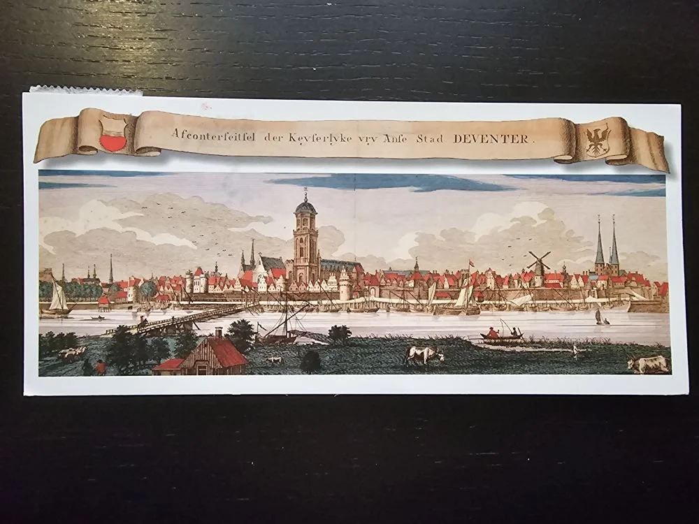 Ein altes, koloriertes Stadtpanorama von Deventer zeigt eine Flusslandschaft mit Brücke, vielen Schiffen, prominenten Kirchtürmen und ländlichem Vordergrund.