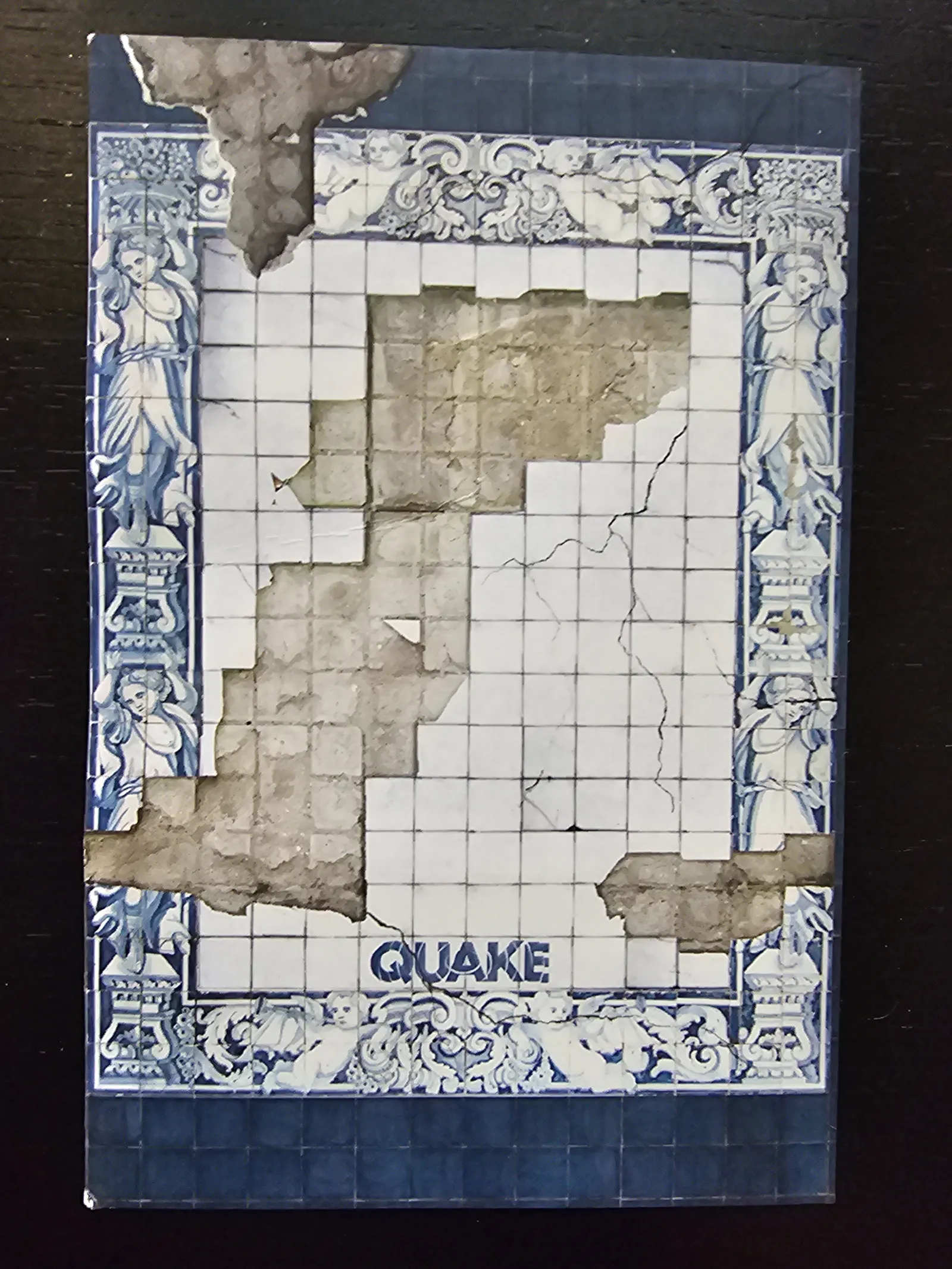 Ein stark zerstörtes blau-weißes Fliesenbild im Azulejos-Stil mit fehlenden Kacheln und Rissen zeigt unten das Wort „QUAKE“.