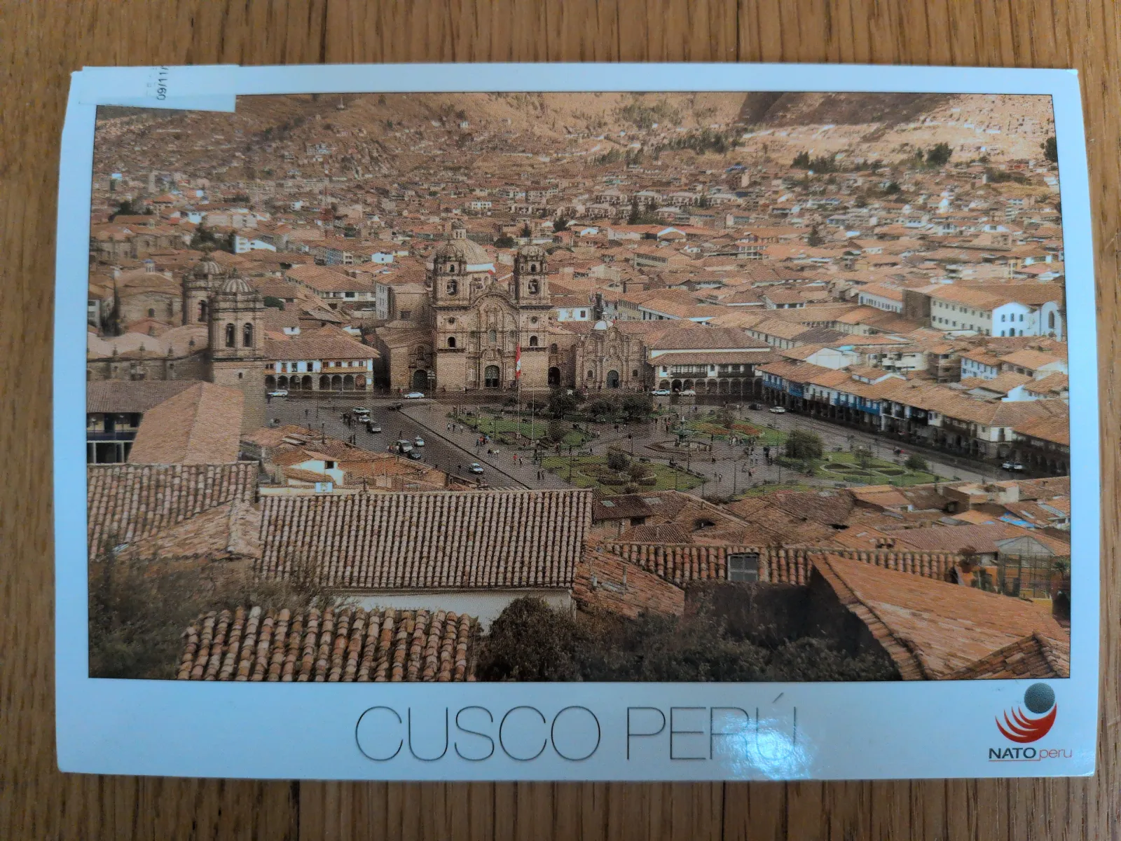 Eine Luftaufnahme zeigt die Stadt Cusco in Peru mit unzähligen roten Ziegeldächern, einem großen Hauptplatz mit Kathedrale und umliegenden Bergen.