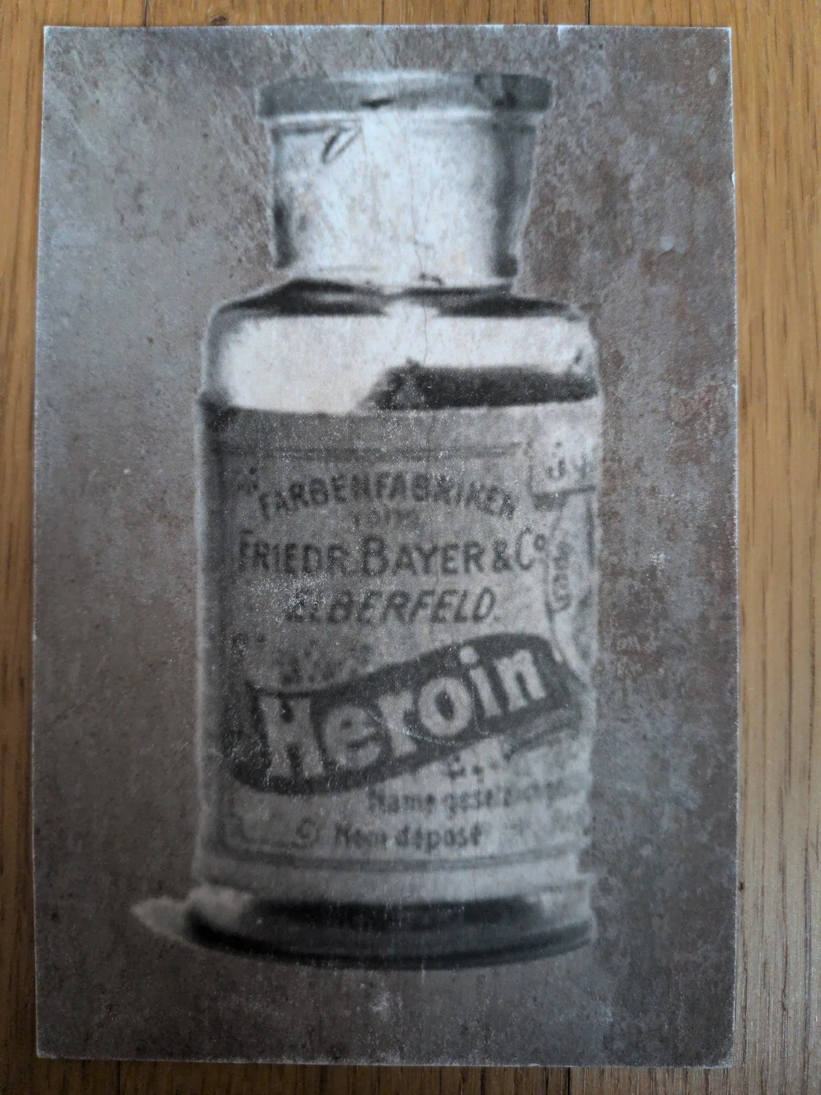 Ein verblasstes Schwarz-Weiß-Bild zeigt eine historische Flasche mit der Aufschrift „Heroin“ von Bayer.