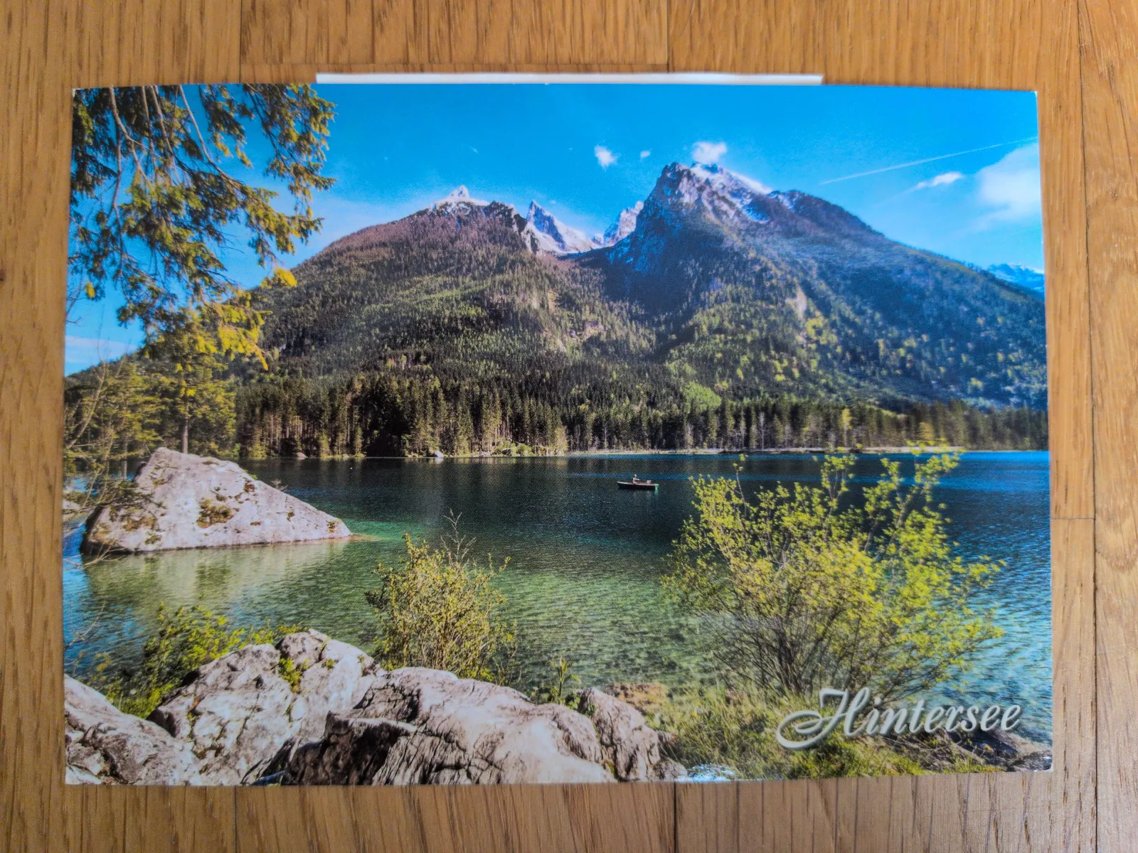 Der klare Hintersee mit einem kleinen Boot ist umgeben von bewaldeten Bergen und schneebedeckten Gipfeln.