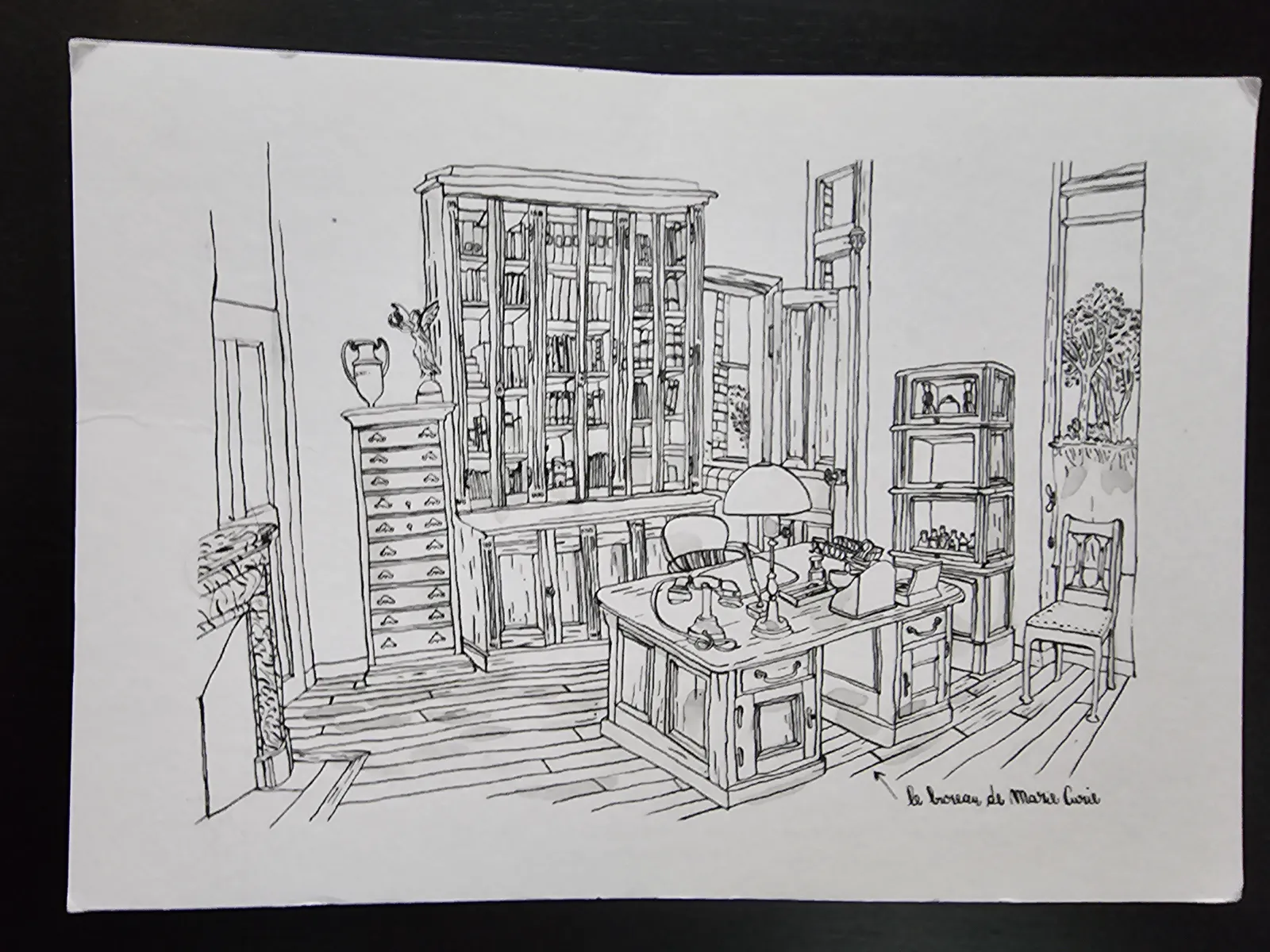 Eine Schwarz-Weiß-Strichzeichnung zeigt ein detailreiches, altmodisches Büro mit einem Schreibtisch, Bücherregalen und Fenstern, das als Marie Curies Arbeitszimmer beschriftet ist.