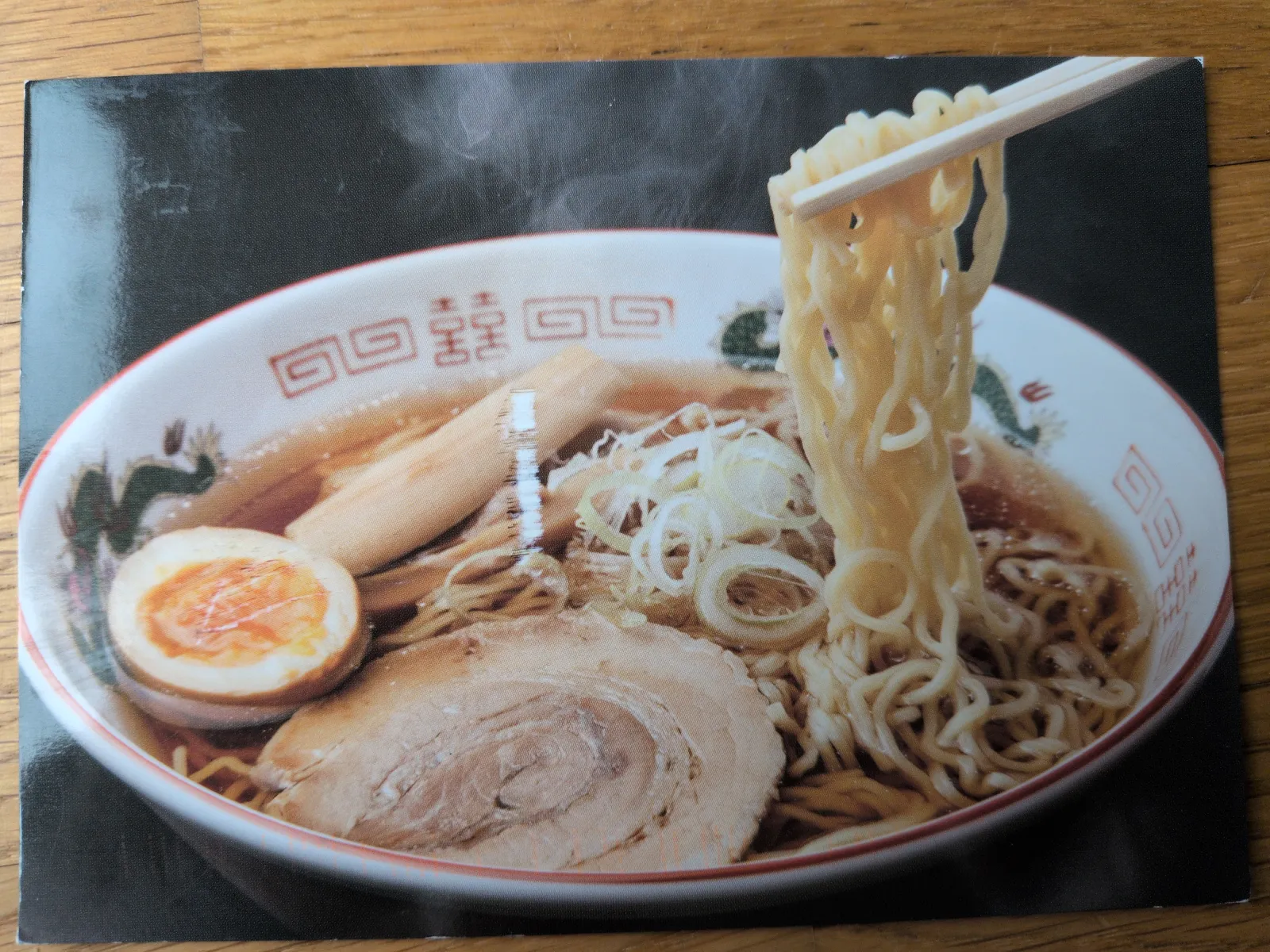 Eine dampfende Schüssel Ramen, aus der Essstäbchen Nudeln heben, mit Schweinefleisch, Ei und Gemüse.