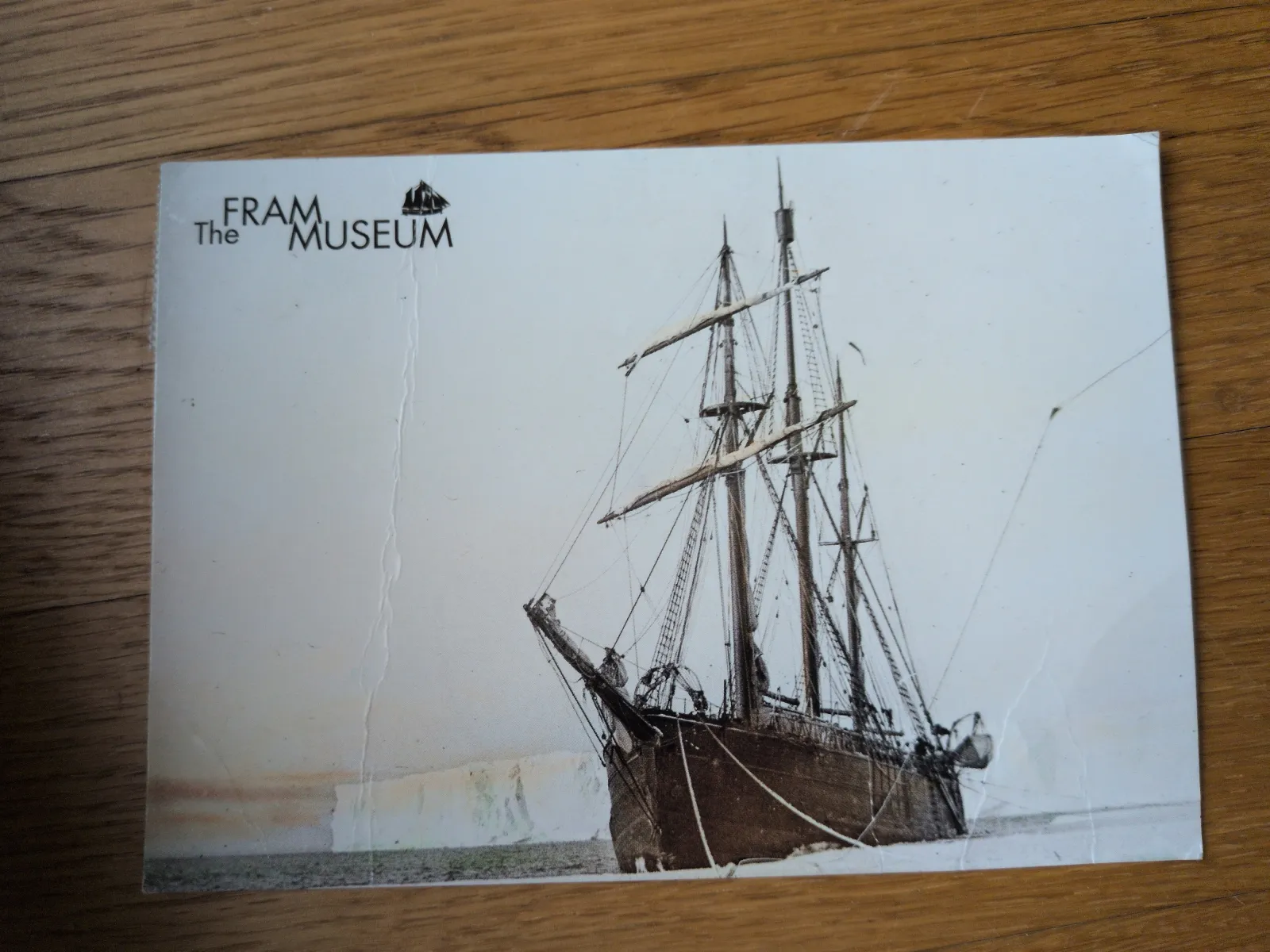 Eine historische Aufnahme zeigt das Segelschiff Fram im Packeis vor einer Eiswand, mit dem Museumslogo oben links.