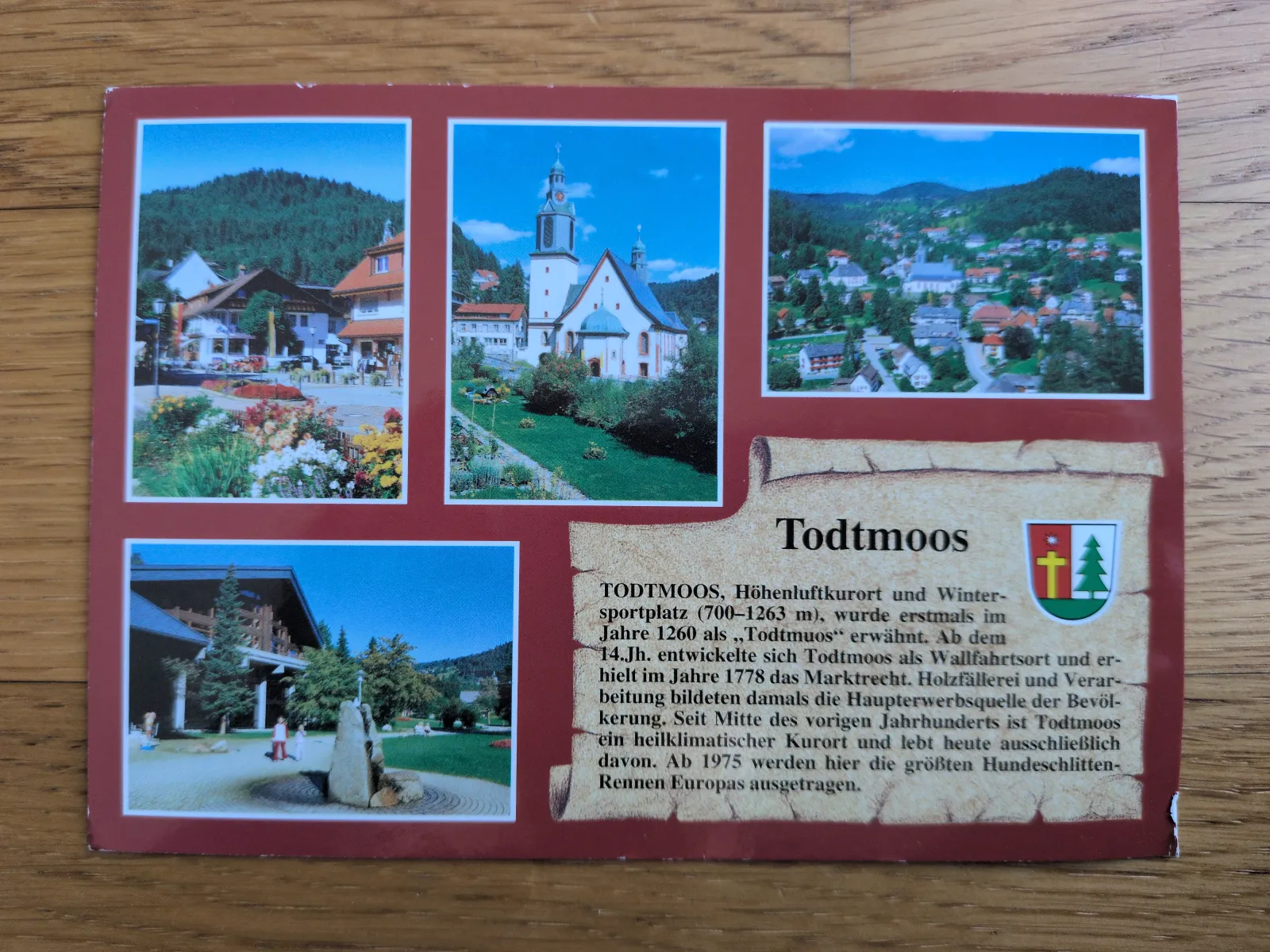 Eine Postkarte präsentiert den Schwarzwaldort Todtmoos in mehreren Bildern mit seiner Kirche, Häusern und grüner Landschaft, begleitet von einem erklärenden Text.
