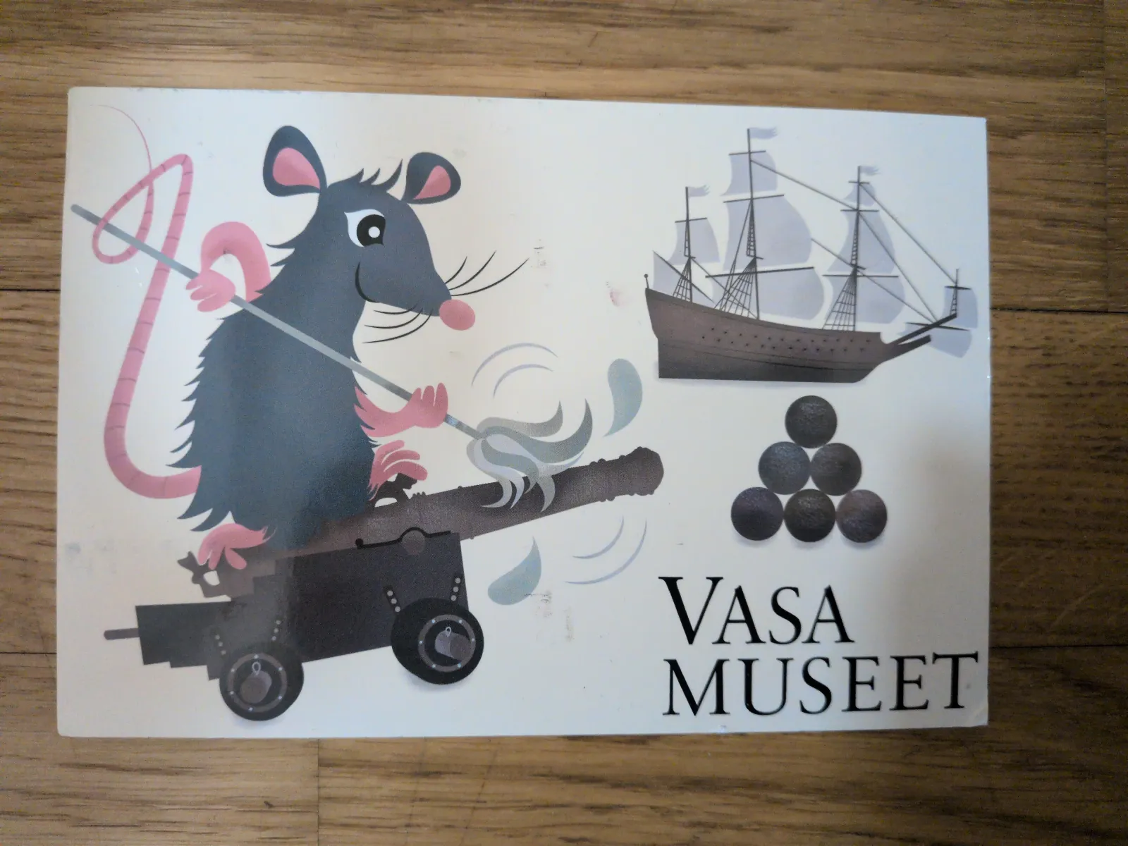 Eine Cartoon-Ratte mit rosa Ohren und Schwanz lädt eine Kanone, daneben sind ein Segelschiff, Kanonenkugeln und der Schriftzug „VASA MUSEET“.