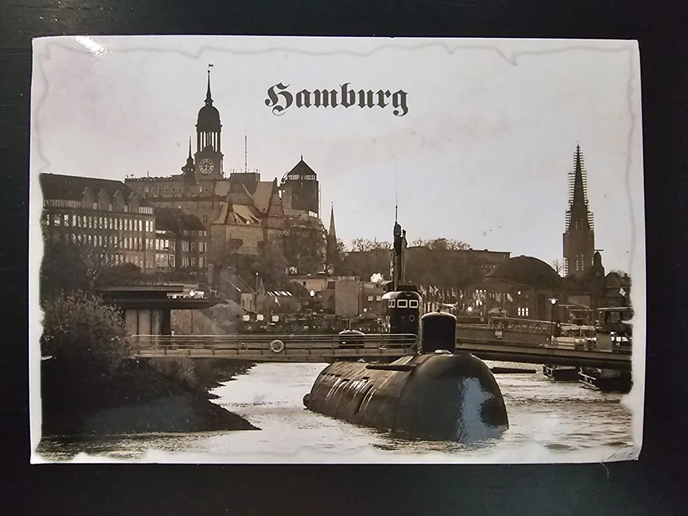 Eine sepiafarbene Postkarte zeigt ein U-Boot im Wasser vor der Hamburger Stadtkulisse mit hohen Türmen.