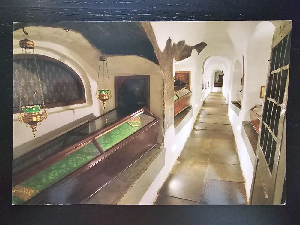 Ein langer, gewölbter Gang mit Steinboden und weißen Wänden, gesäumt von Vitrinen mit Artefakten wie einem grünen Tuch und beleuchtet von hängenden Lampen.