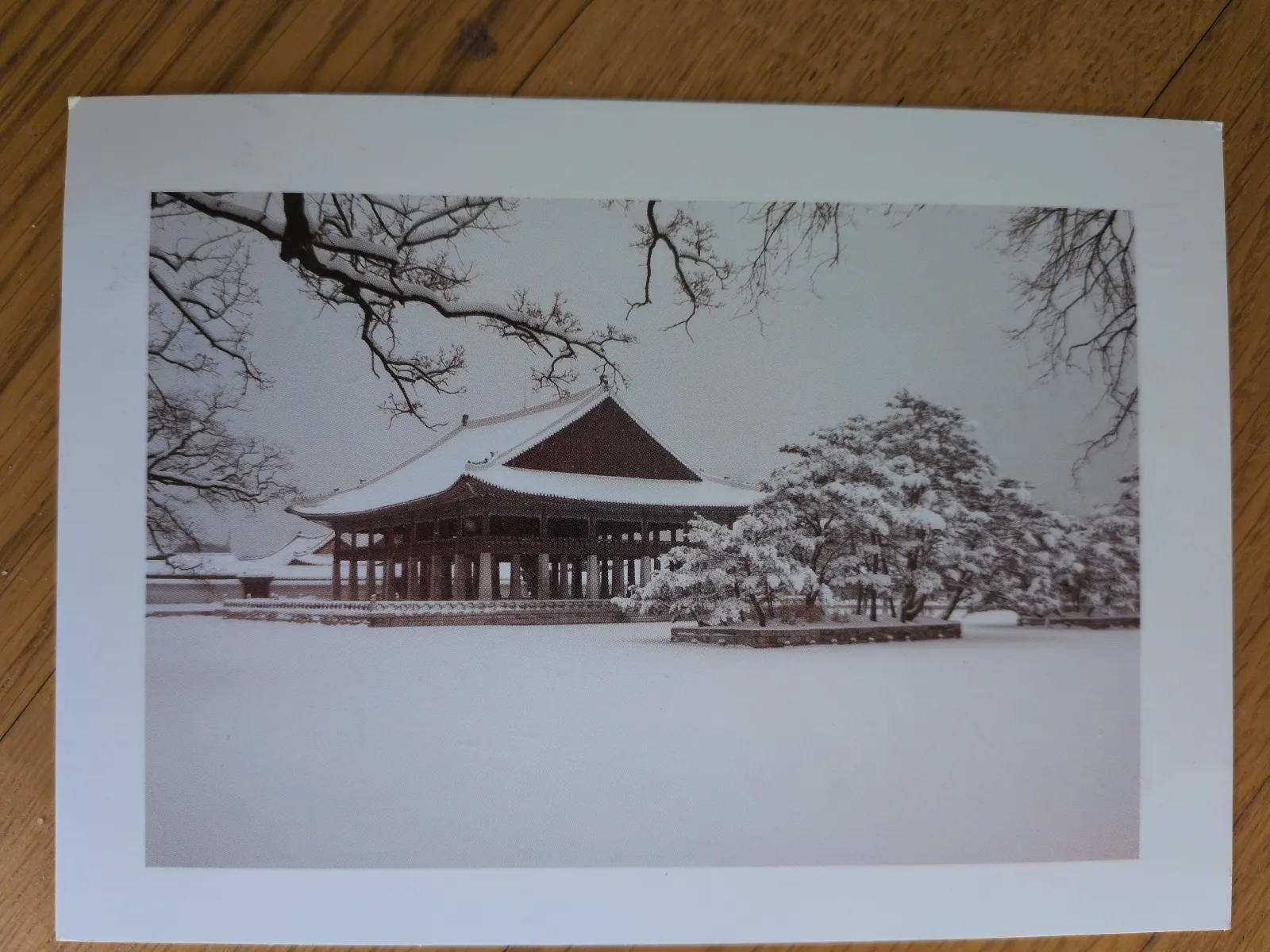 Eine tief verschneite Winterlandschaft mit einem traditionellen ostasiatischen Holzgebäude, umgeben von kahlen und schneebedeckten Bäumen.