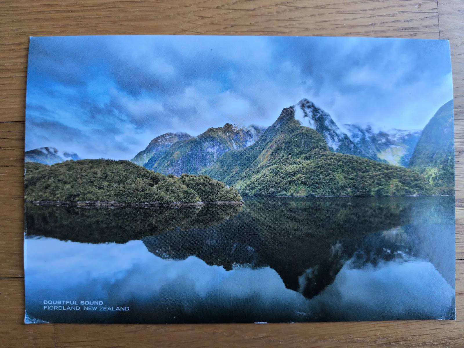Eine dramatische Fjordlandschaft mit bewaldeten Bergen, deren Gipfel in Wolken liegen und sich im spiegelglatten Wasser abbilden.